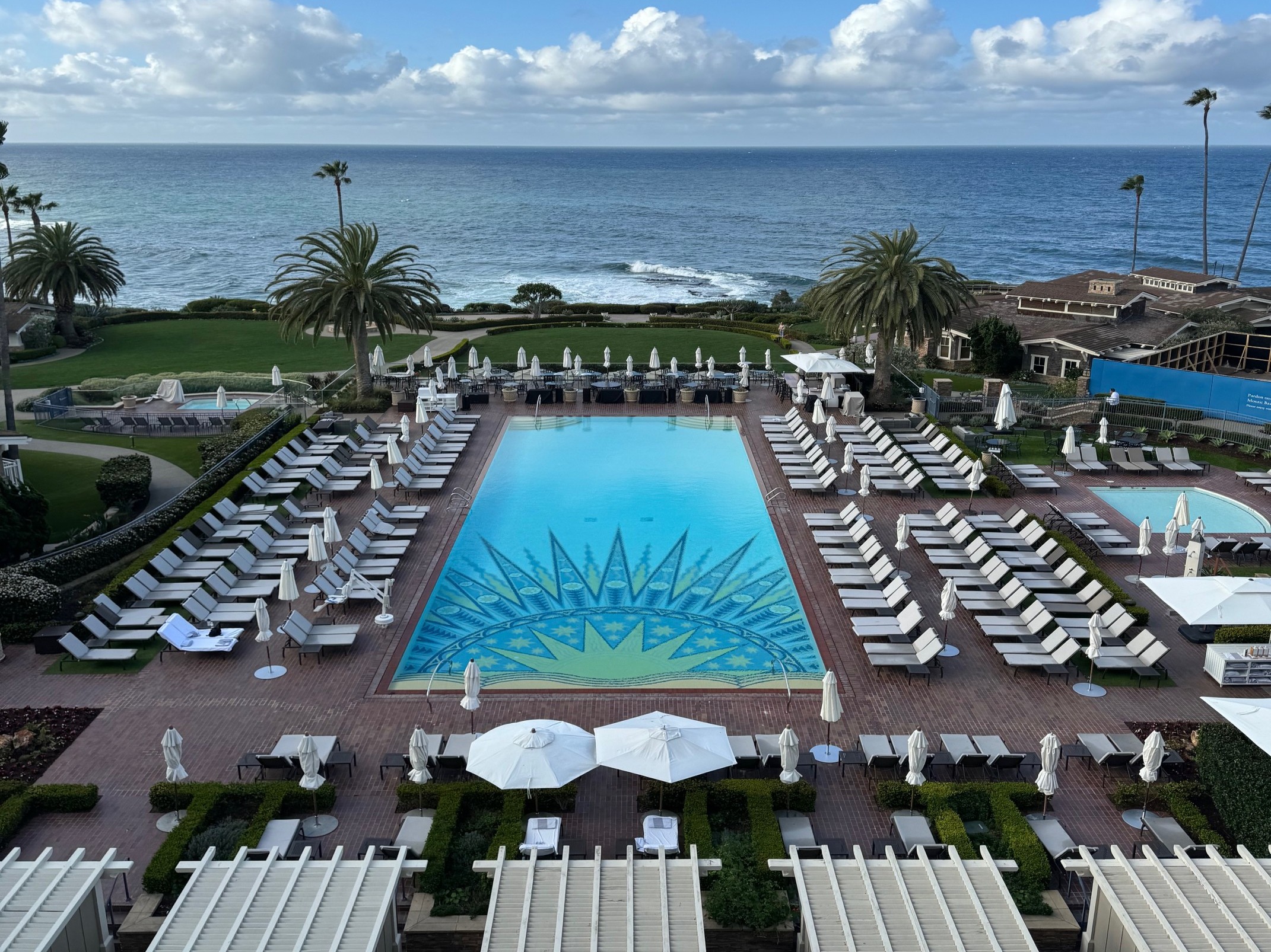 A luxurious poolside retreat with white sun loungers and umbrellas, overlooking a tranquil sea.