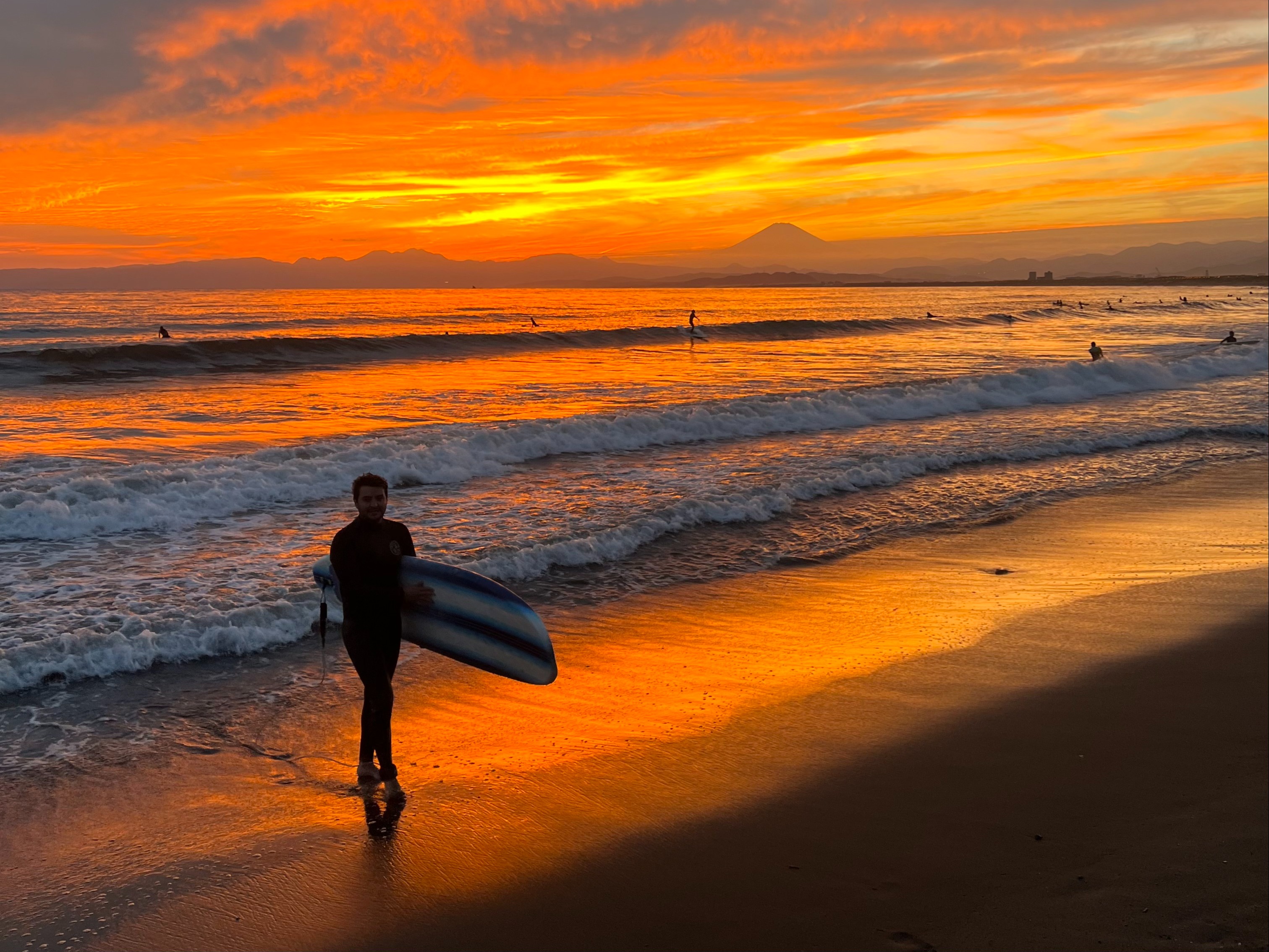 A silhouette of a surfer holding a board against a stunning beach sunset.