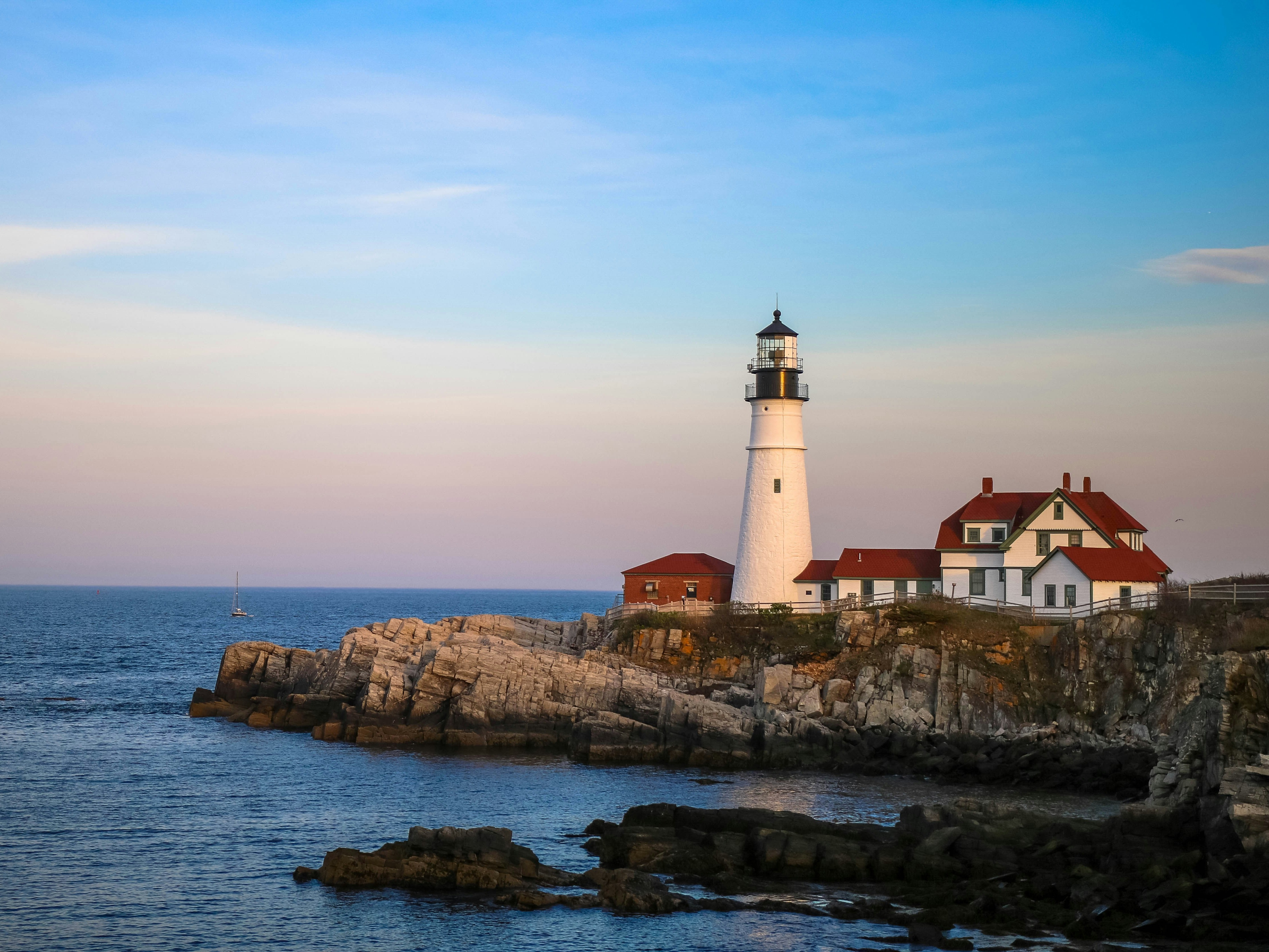 A lighthouse and red-roofed building on a rocky cliffside during the sunset