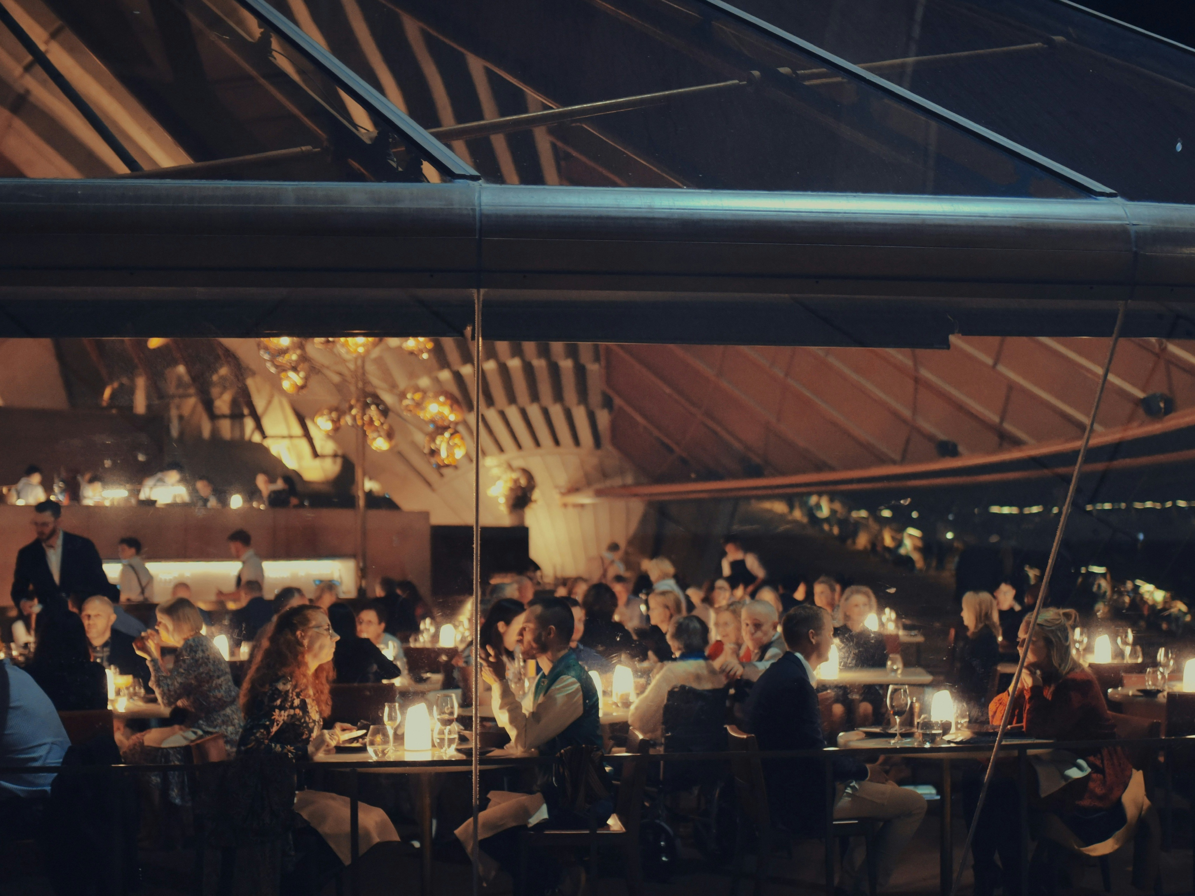The image shows a lively restaurant scene at night with guests enjoying their meals in a cozy ambiance.
