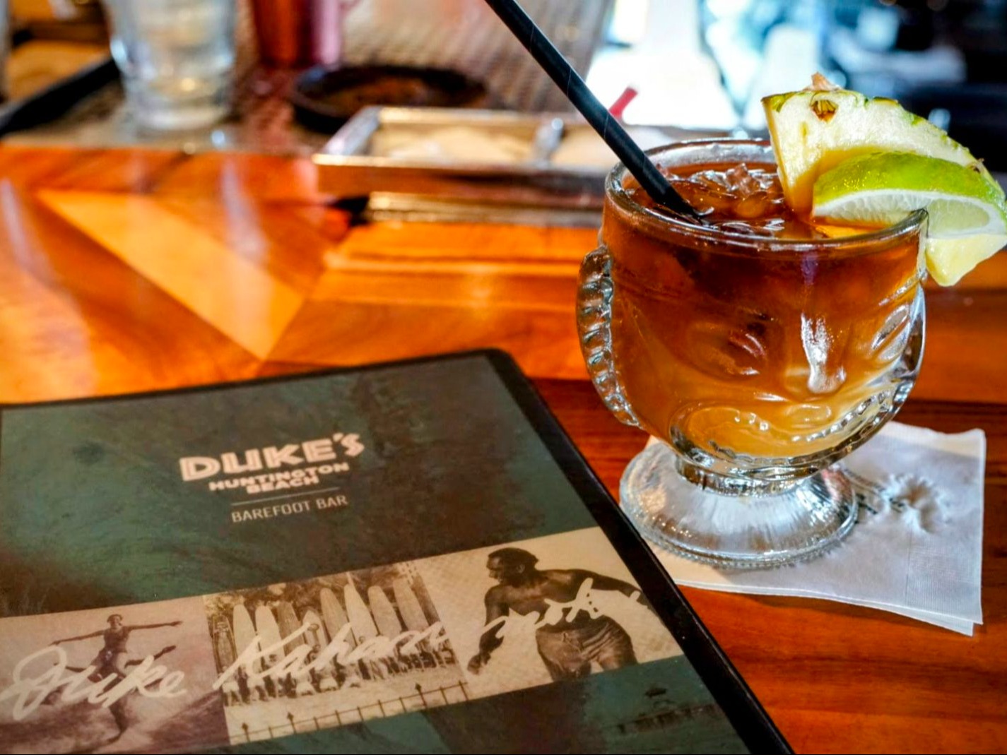 The image features a menu from Duke’s Huntington Beach, set against a blurred backdrop suggestive of a relaxed dining experience.