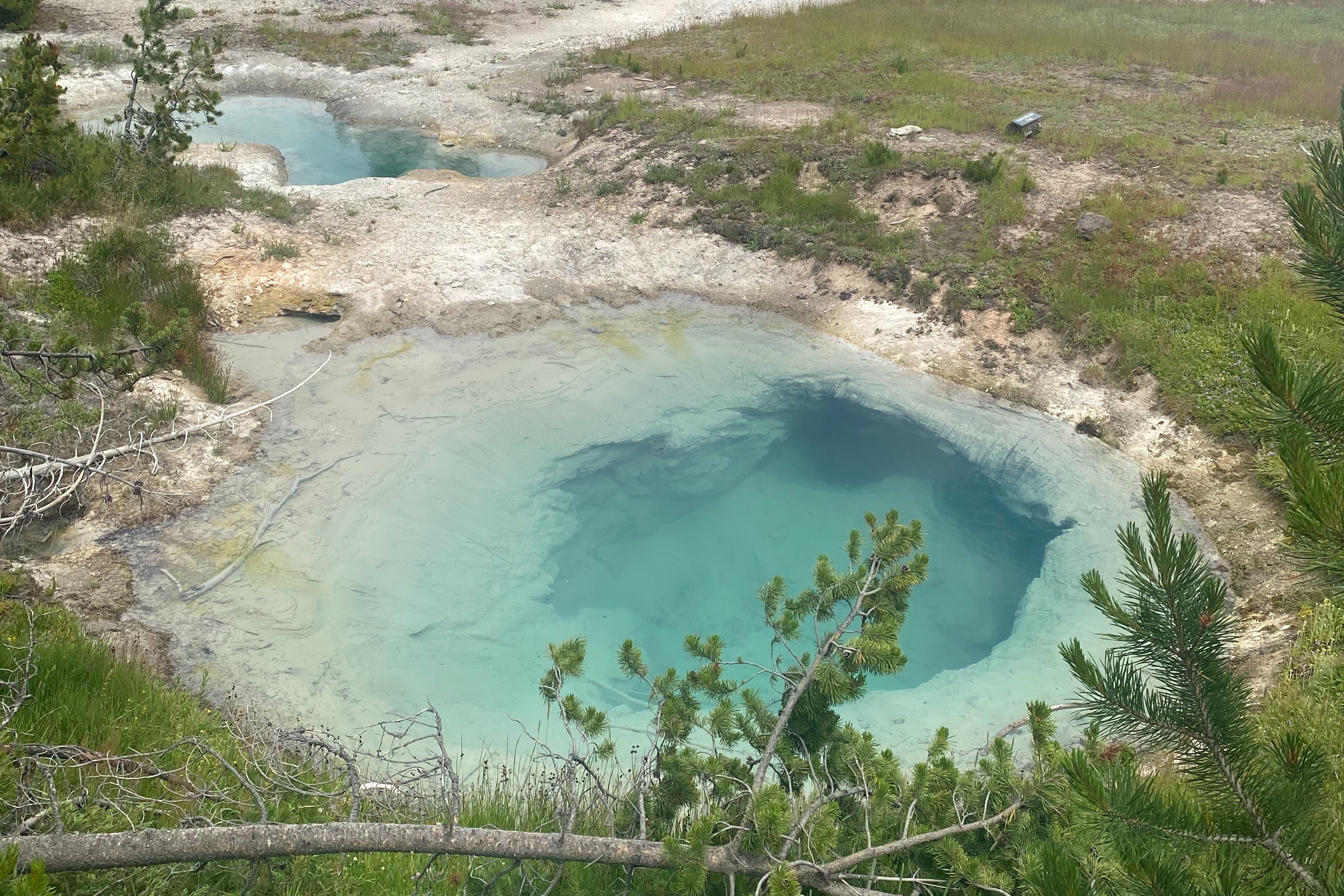 The Abyss Pool is a mesmerizing hot spring with its azure waters bordered by vibrant orange and yellow mineral deposits.