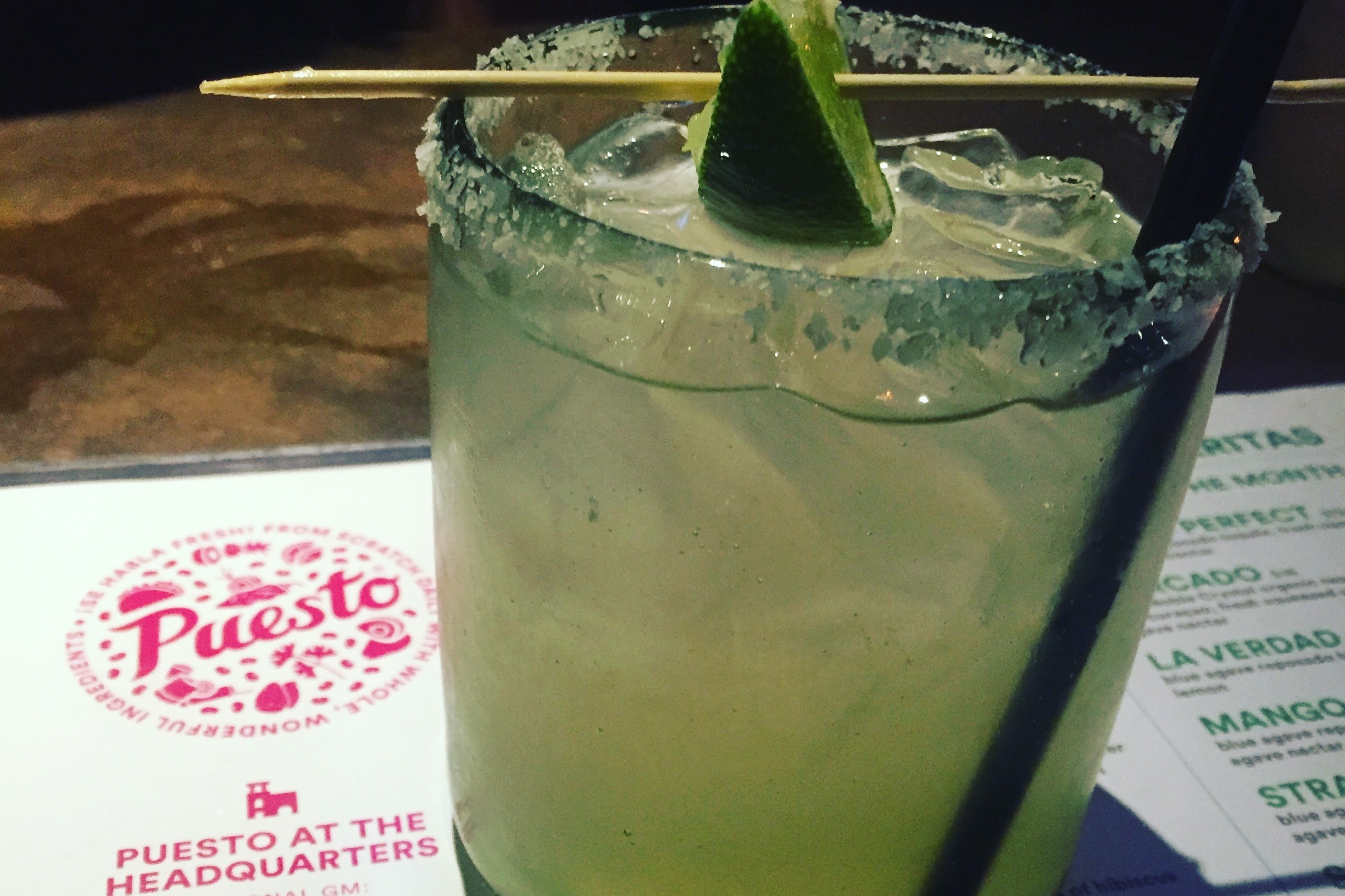 A green drink in a glass, sitting on a menu reading "Puesto"