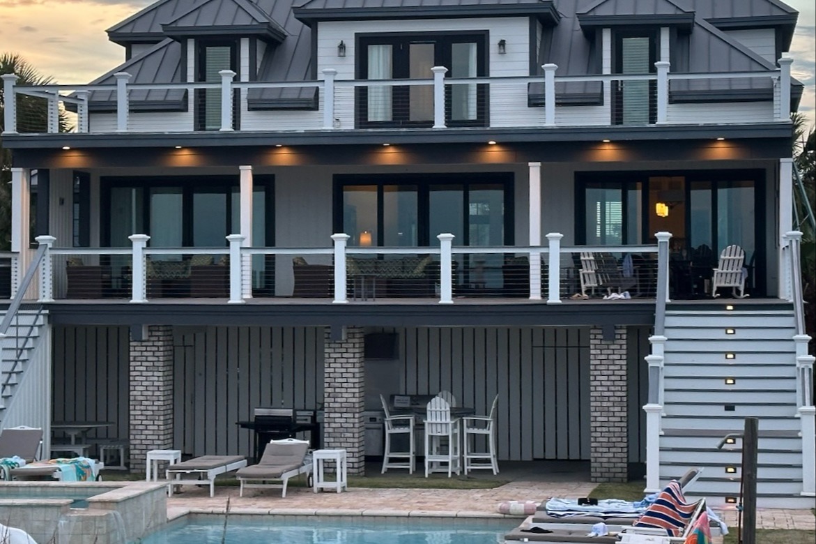 A black and gray three-story home with a pool in front