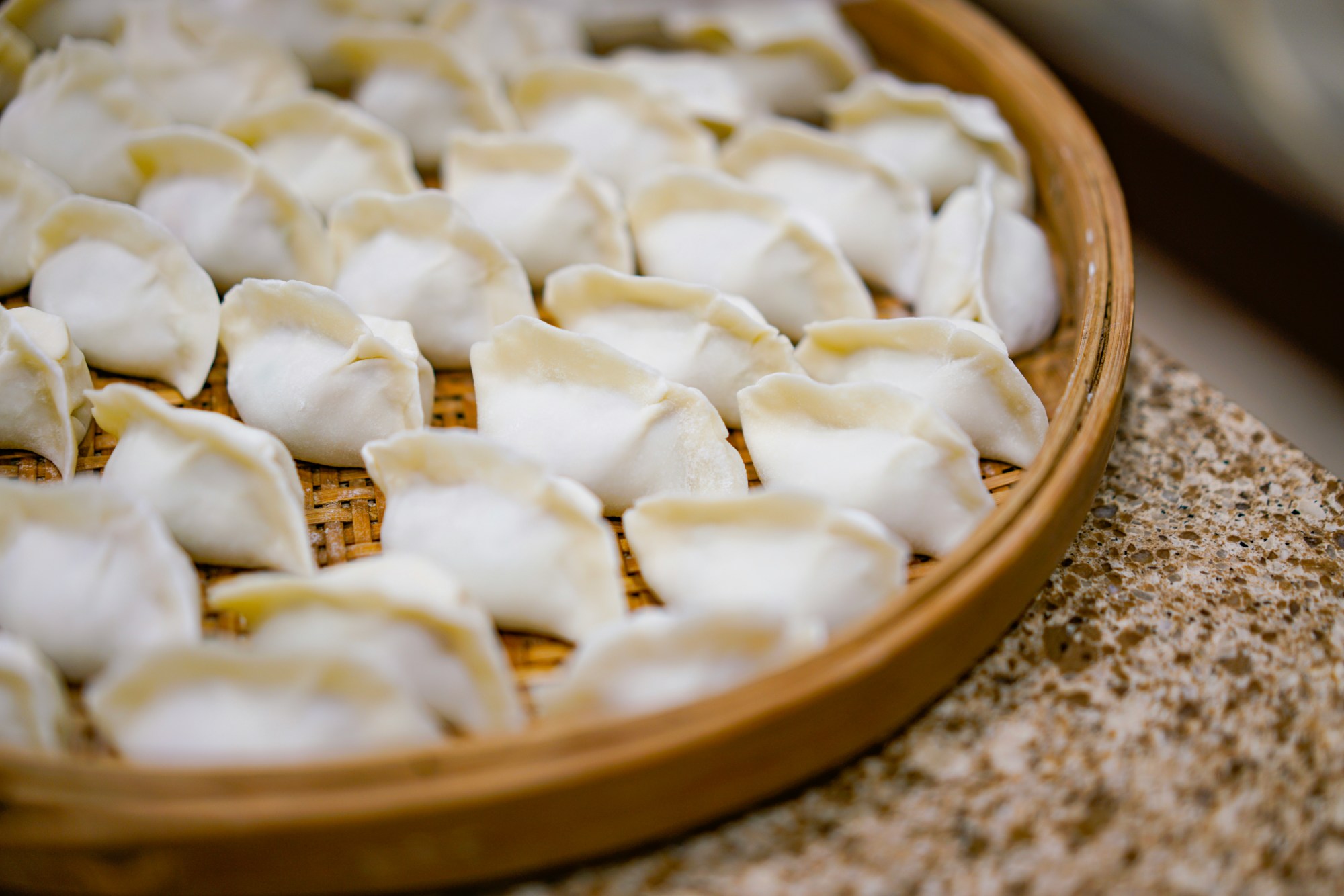 A plate of attentively crafted and hand-pinched dumplings, elegantly placed on a bamboo board, waiting to be steamed.