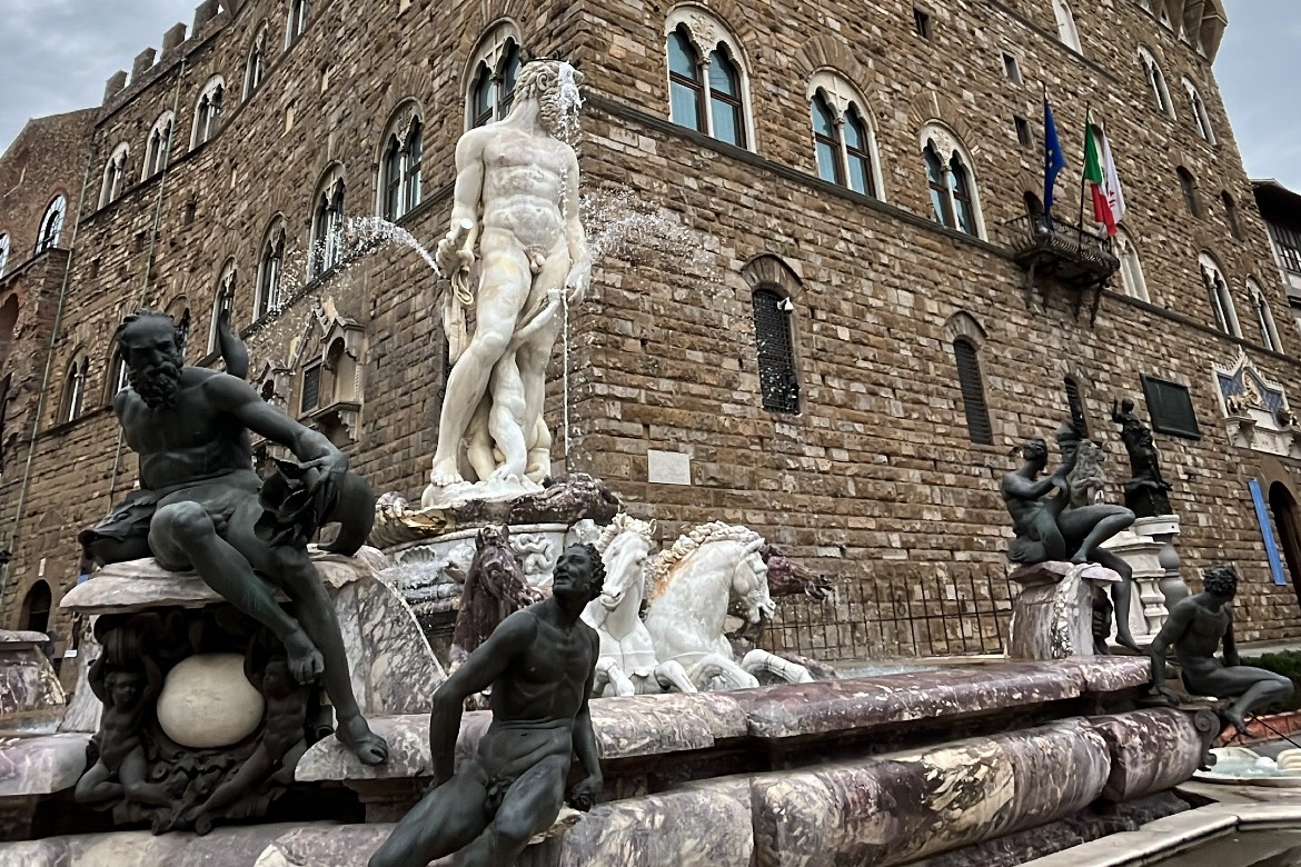 A fountain with statues of men in it, in front of a large brown brick building