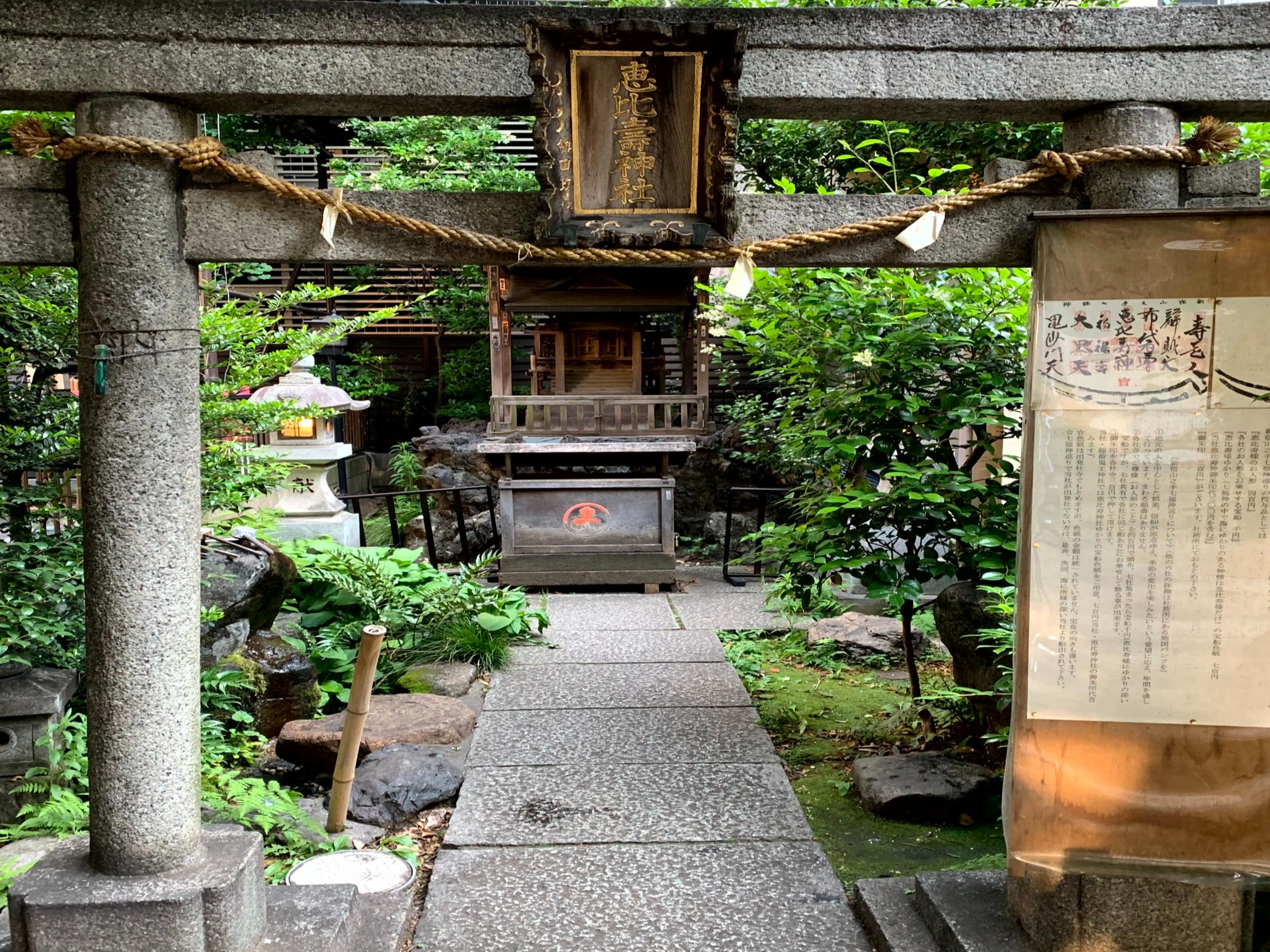A peaceful shrine with traditional Japanese stone structures amidst lush greenery, with a lantern and inscribed plaques adding to the serene ambiance.