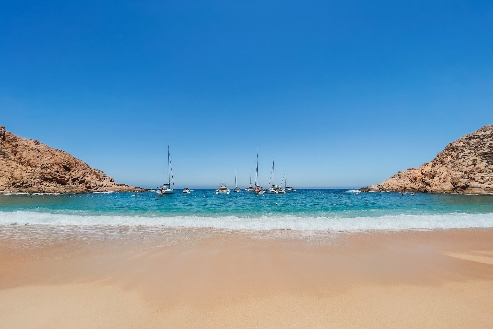 A view from Playa Santa Maria, a beautiful beach with boats sailing and rocky cliffs either side