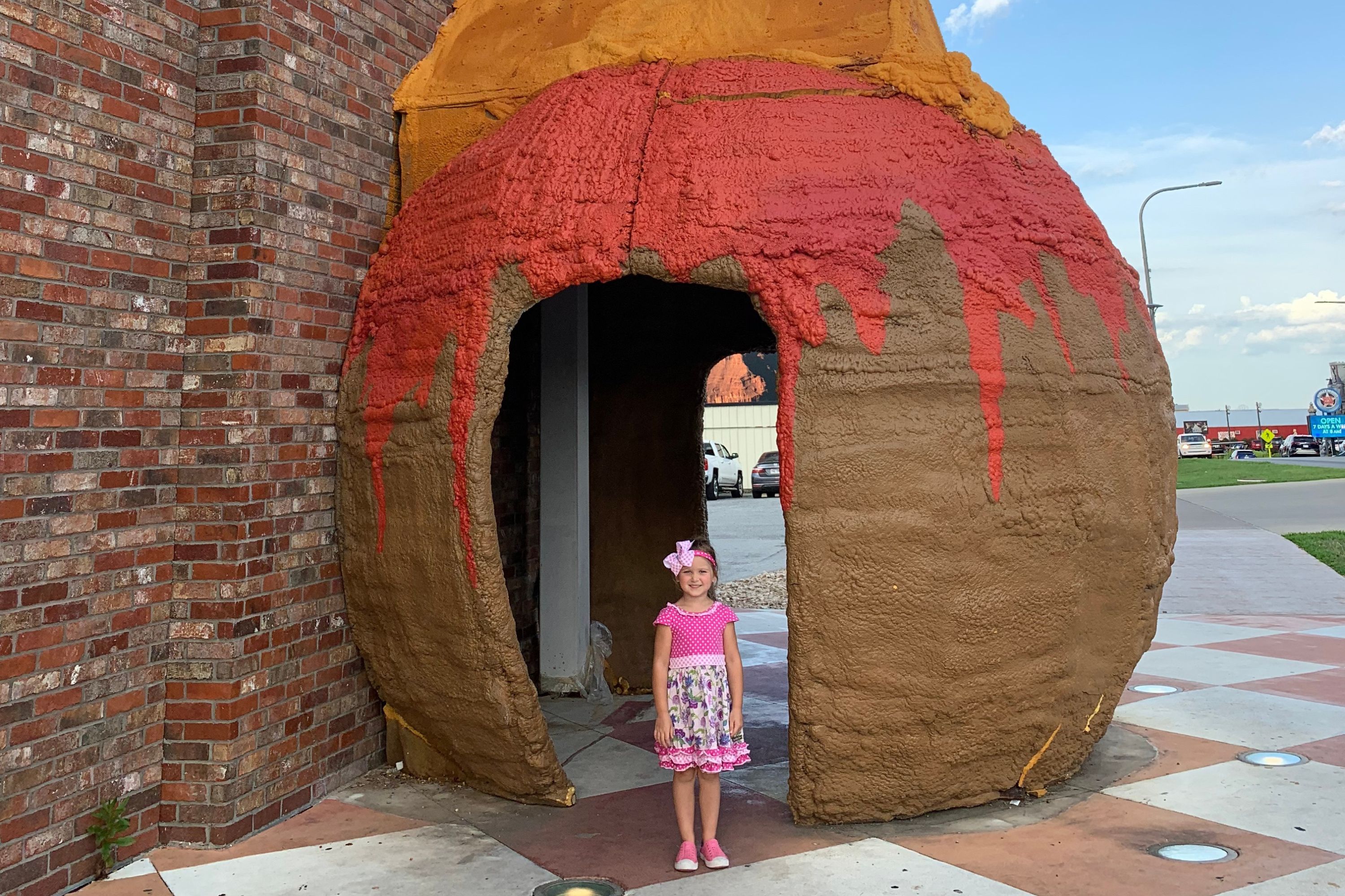 A young child standing in front of a brown, red and orange sculpture with a doorway
