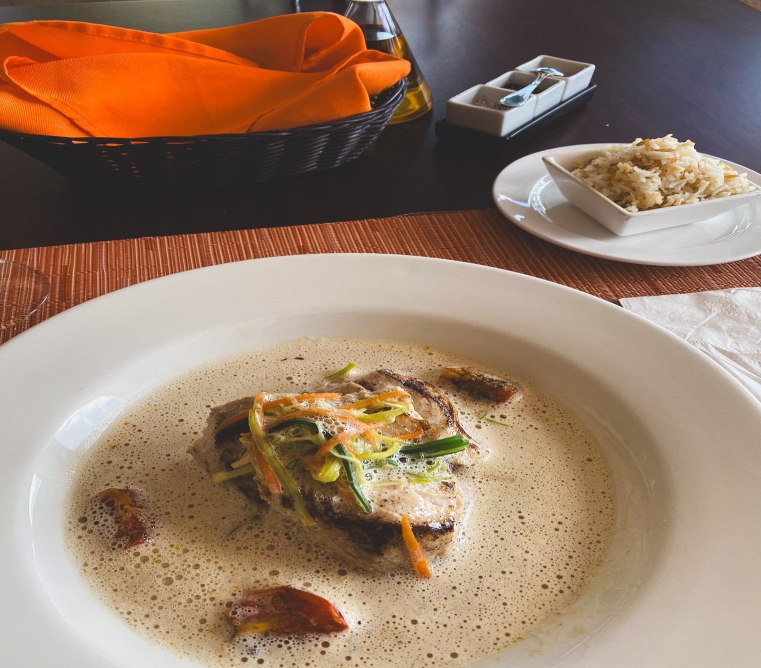 A plate of grilled fish with vegetables, rice and bread is elegantly presented on a wooden table.