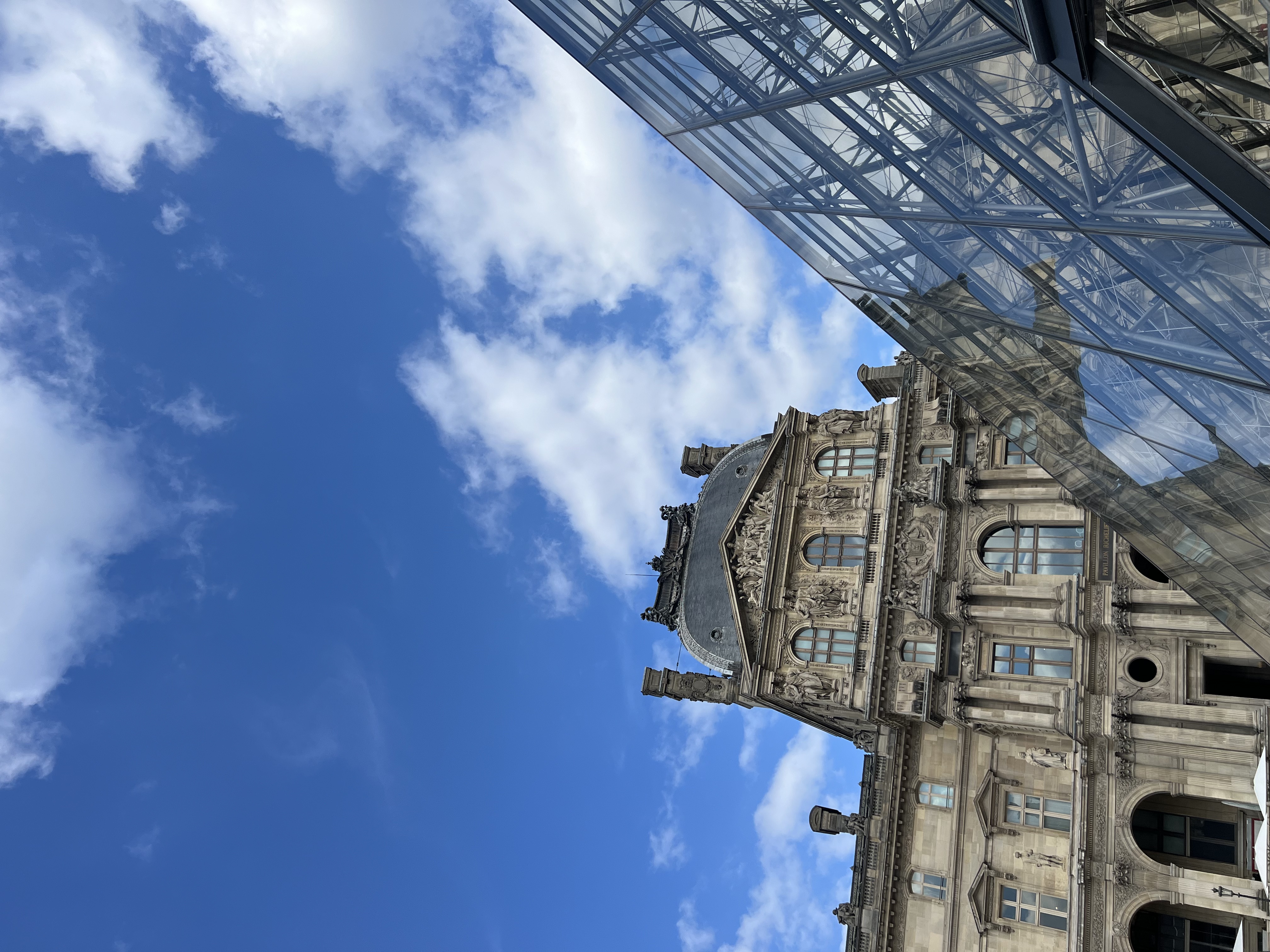 An upward angle of the Louvre on a sunny day with clouds