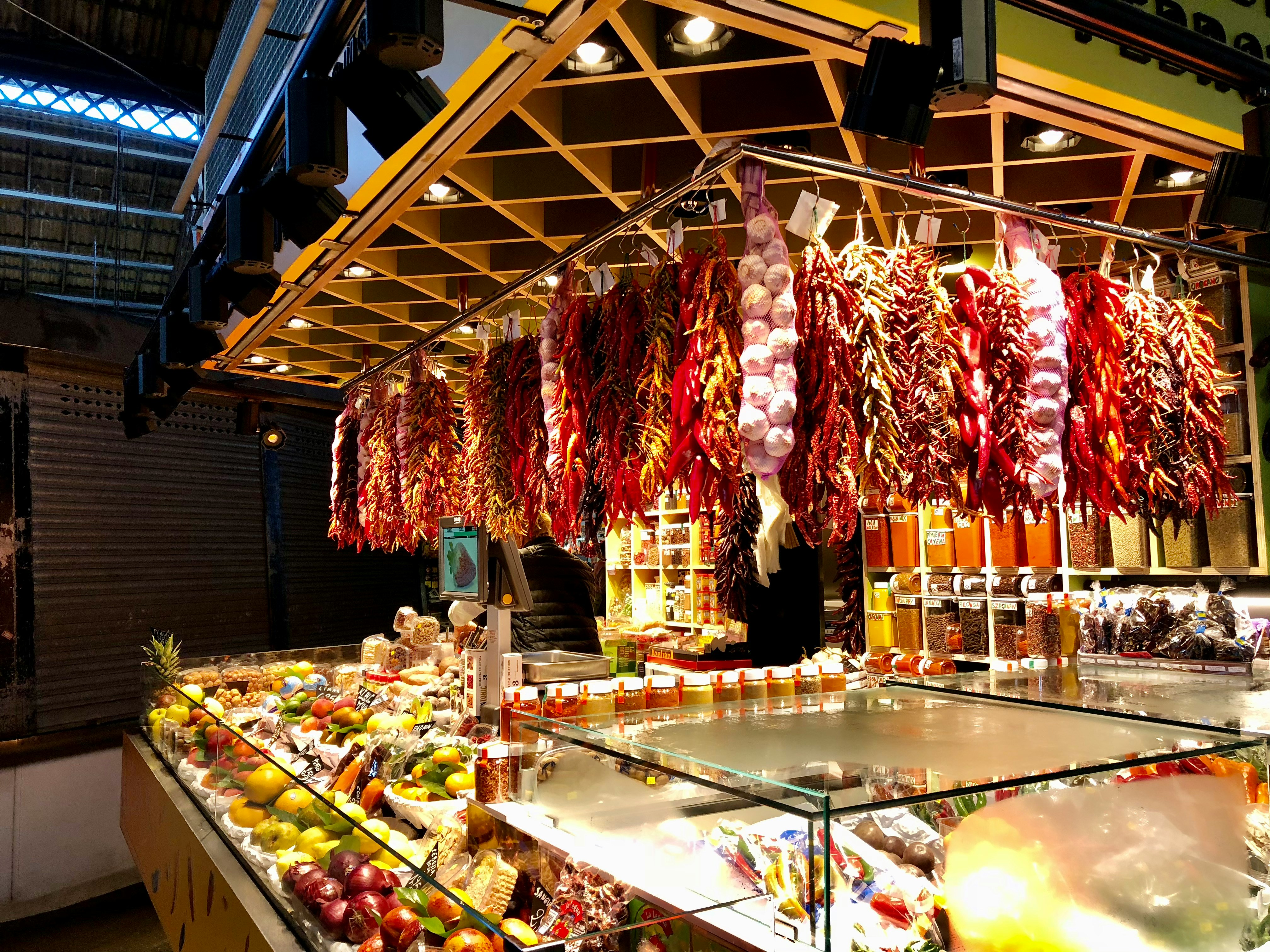 A stall at La Boqueria market, with hanging chilies above a glass counter filled with fruit.