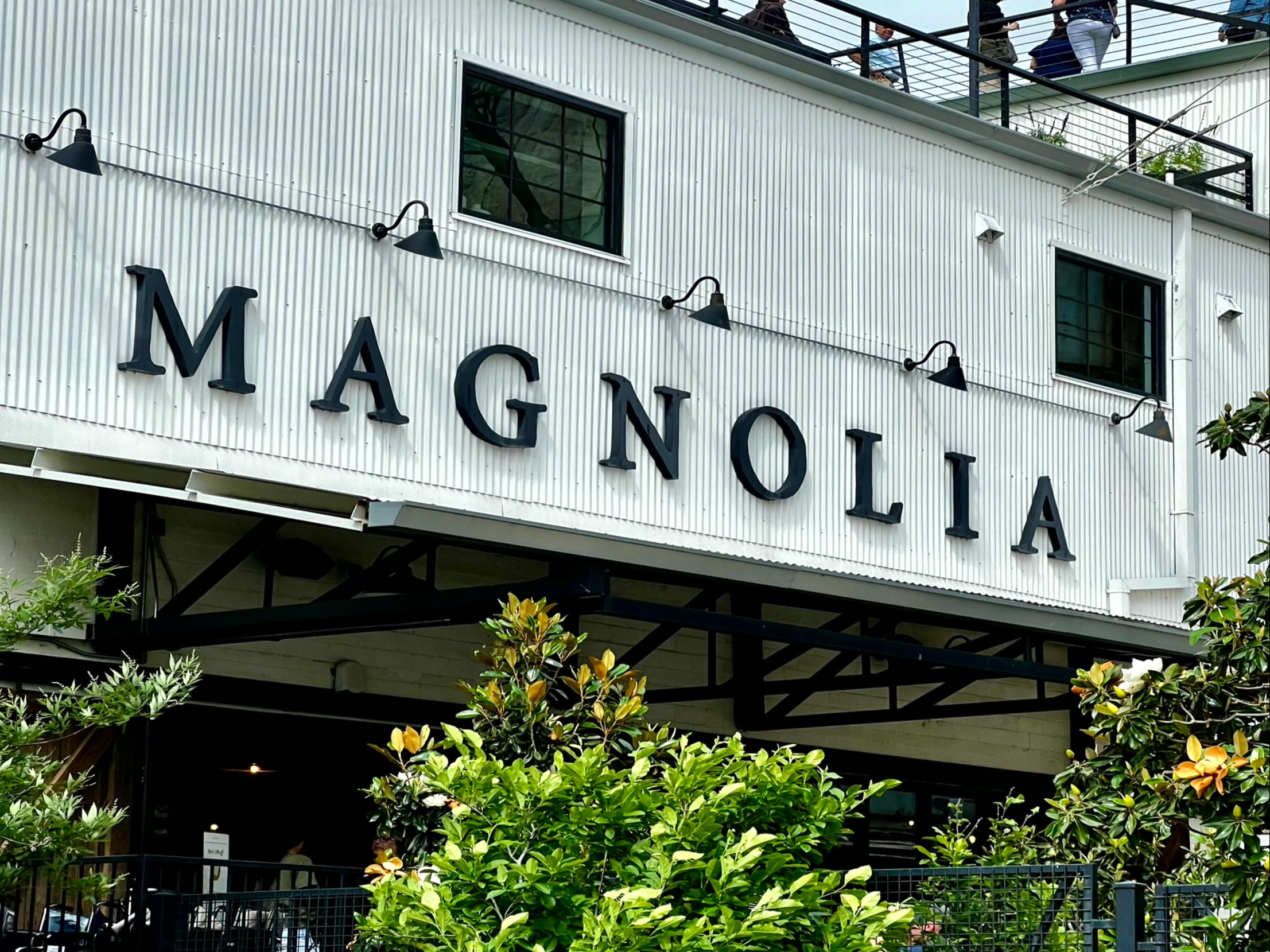 A white building named “MAGNOLIA” with string lights and greenery