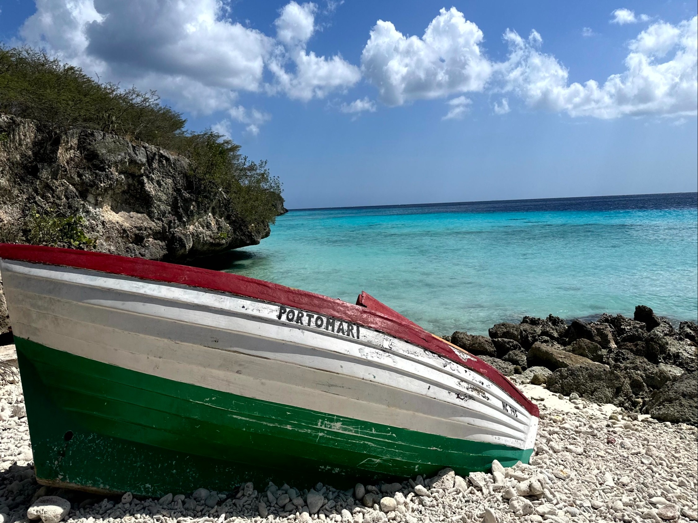 A red, white, and green boat on a rocky beach next to the water during the daytime