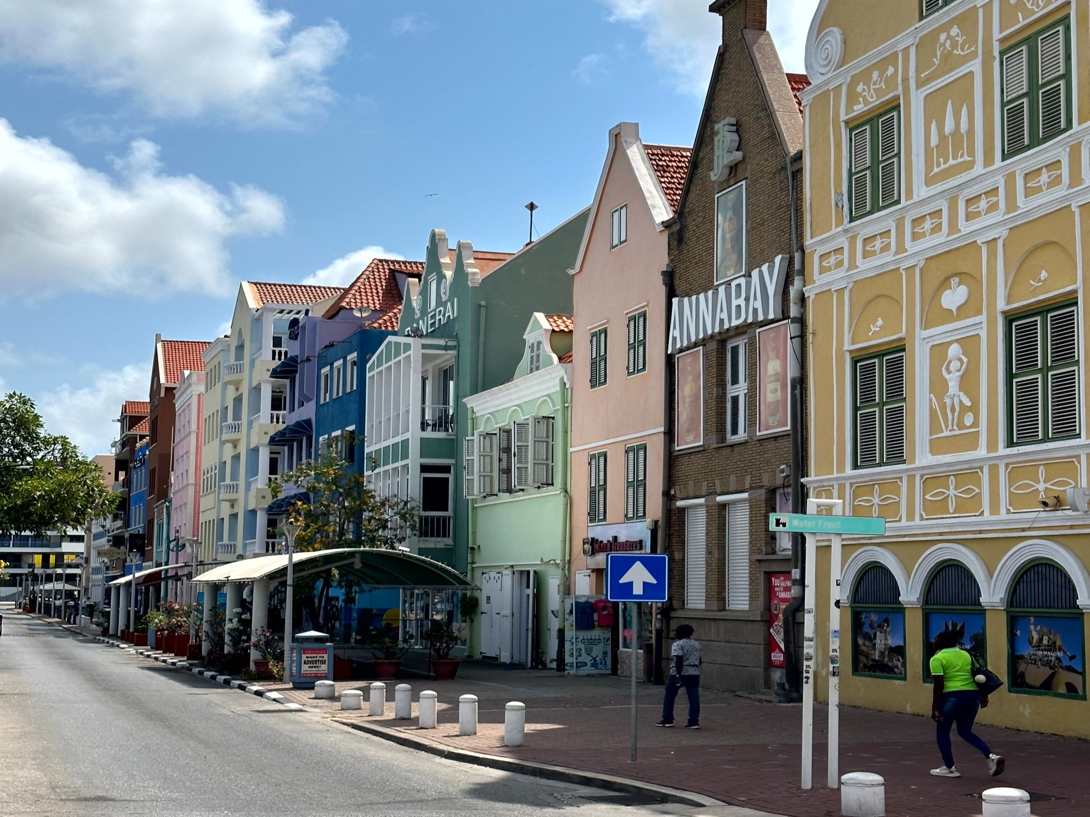 The image presents a vibrant street scene with colorful buildings and a bustling atmosphere under a sunny sky.