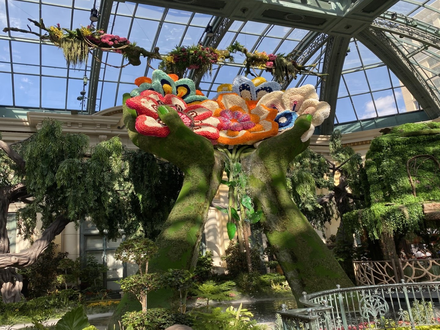 A colorful floral sculpture in an indoor garden under a glass ceiling creates a vibrant and lush visual spectacle.