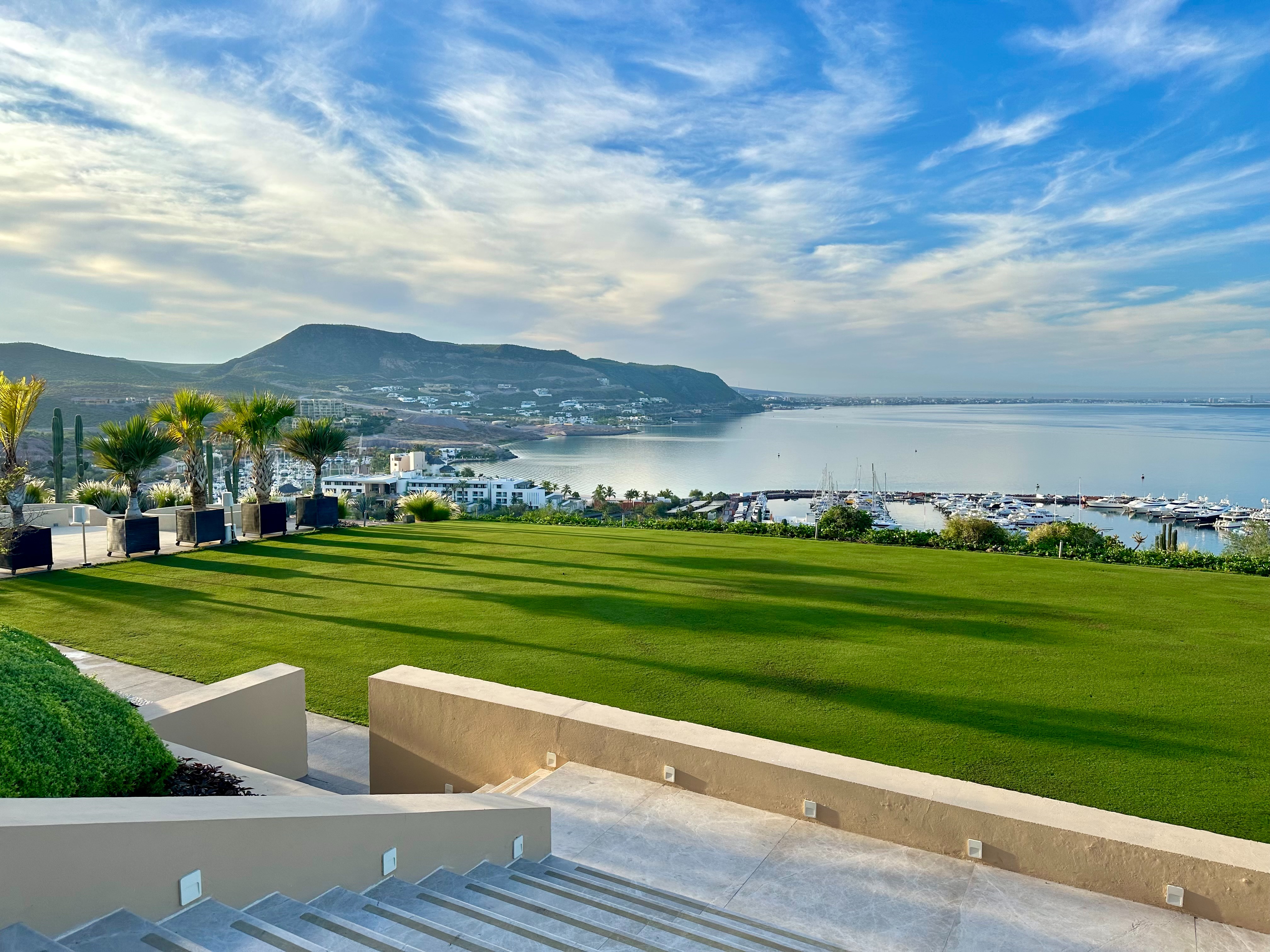 A picturesque coastal view from a grassy terrace overlooking a marina, under a clear blue sky.