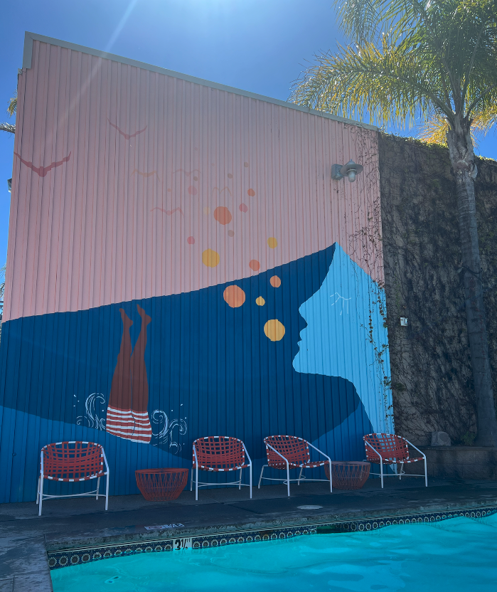 A mural of a person diving into a pool next to a swimming pool with red chairs lined up next to it.