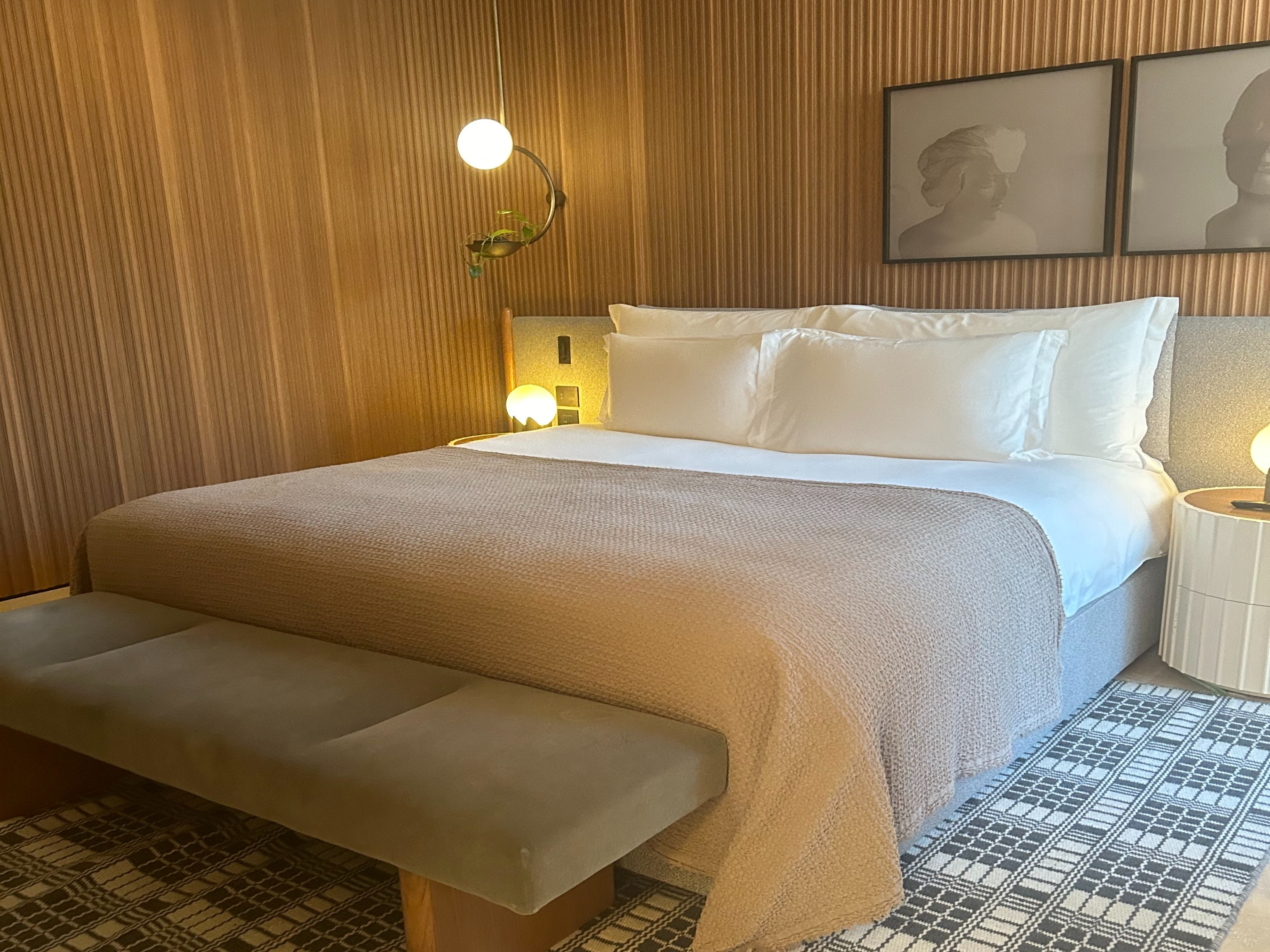 The image features a stylish bedroom with a neatly made bed, framed pictures above the headboard, and a bench at the foot, creating a serene and inviting atmosphere.