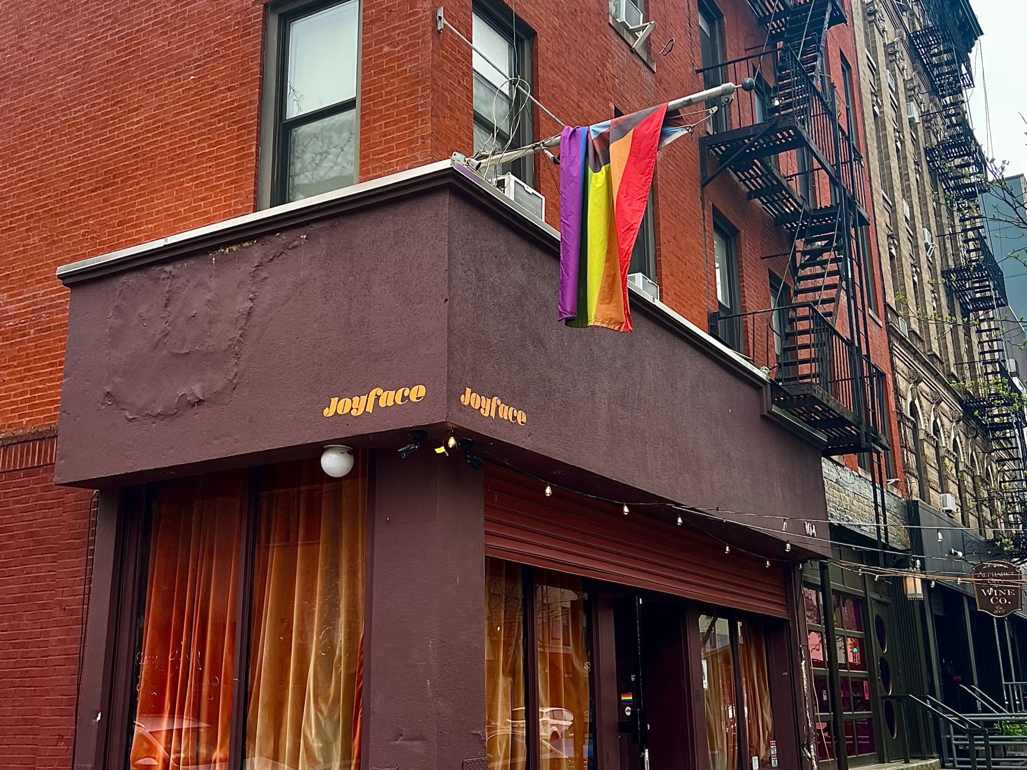 Red building of Joyface bar with LGBT flag hanging from it.