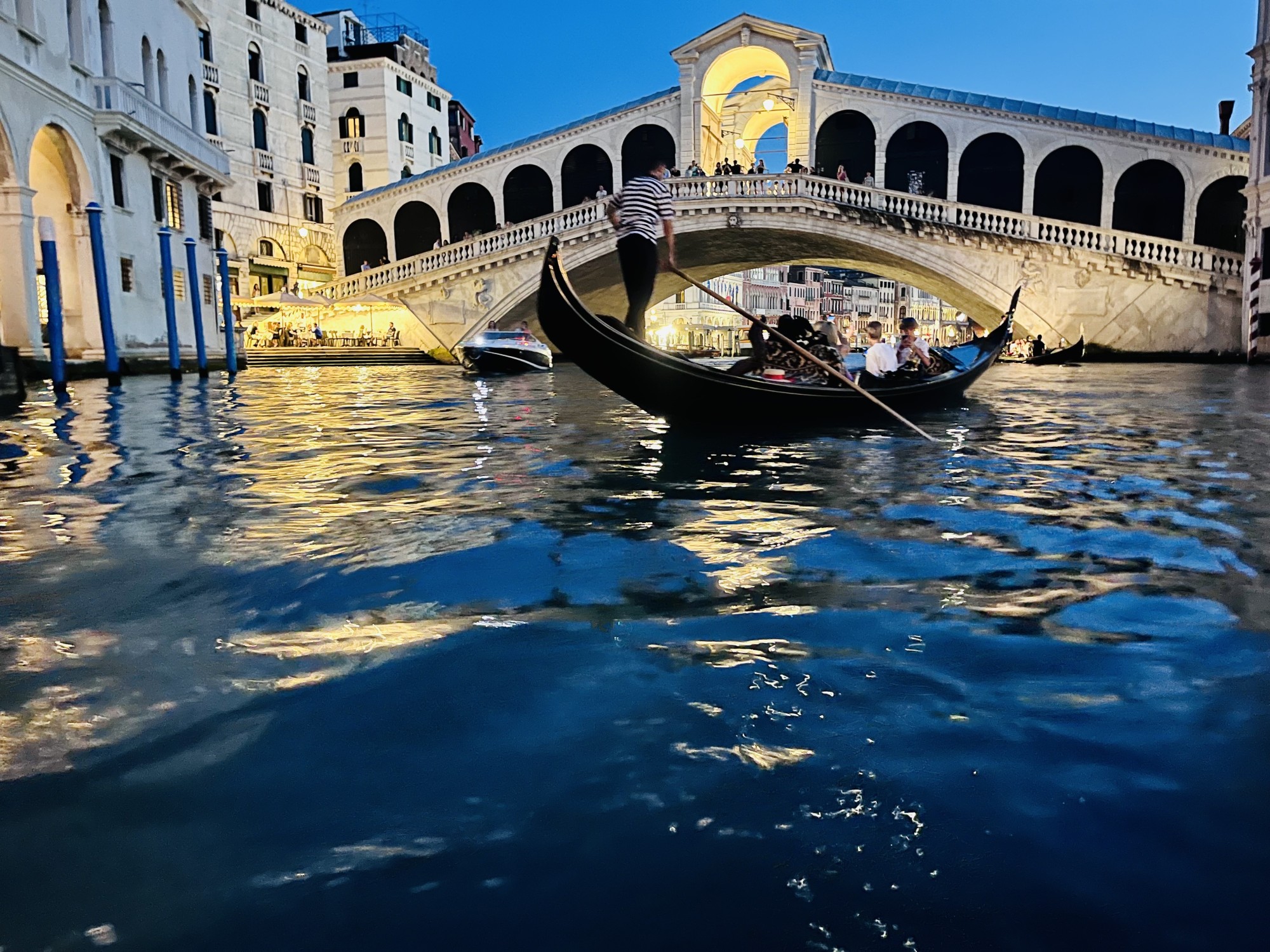 A point of view perspective of a group of travelers on a gondola, with a bridge in the background at dusk.
