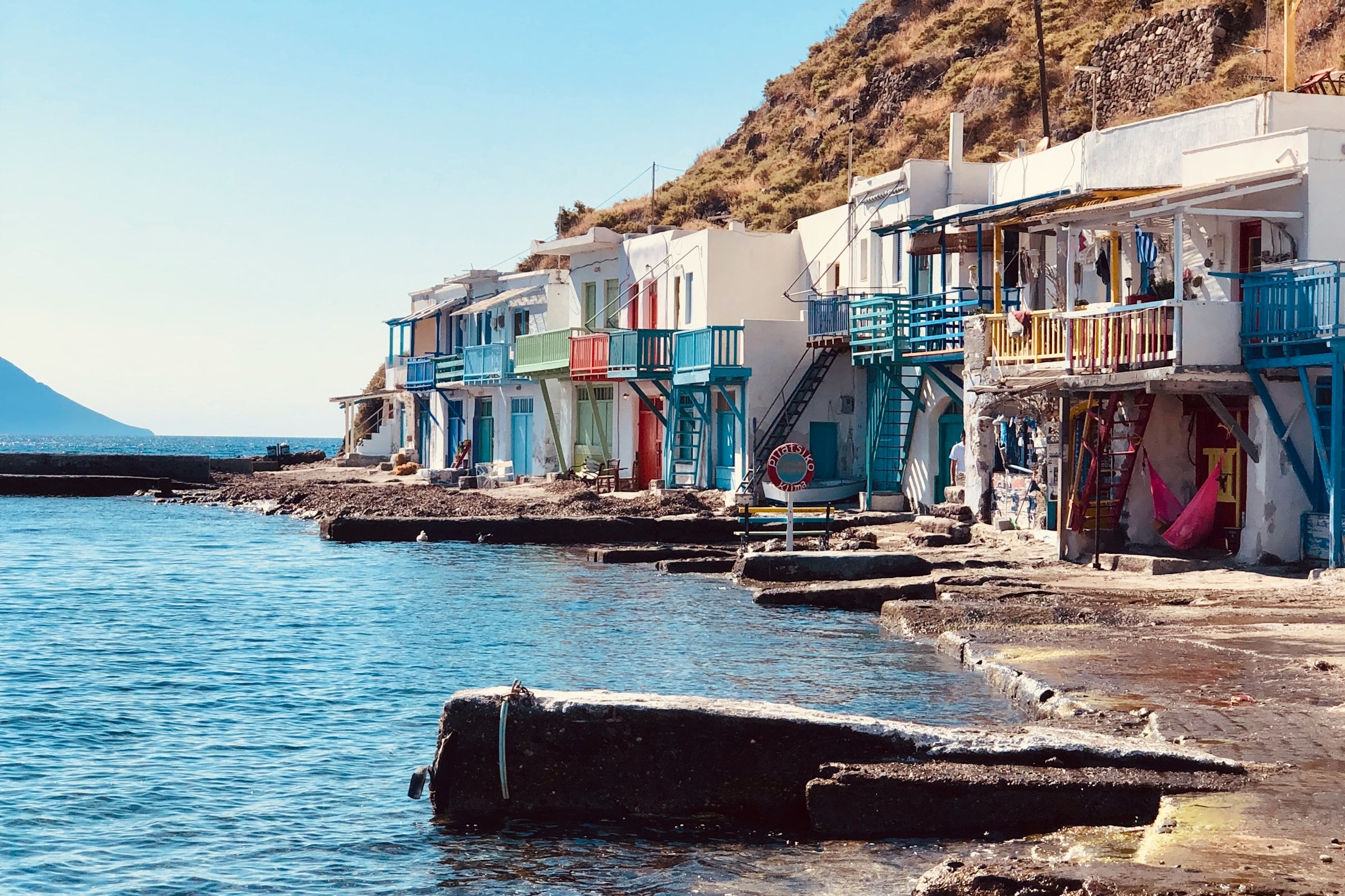 A row of white houses with colorful balconies and stairs next to a blue body of water