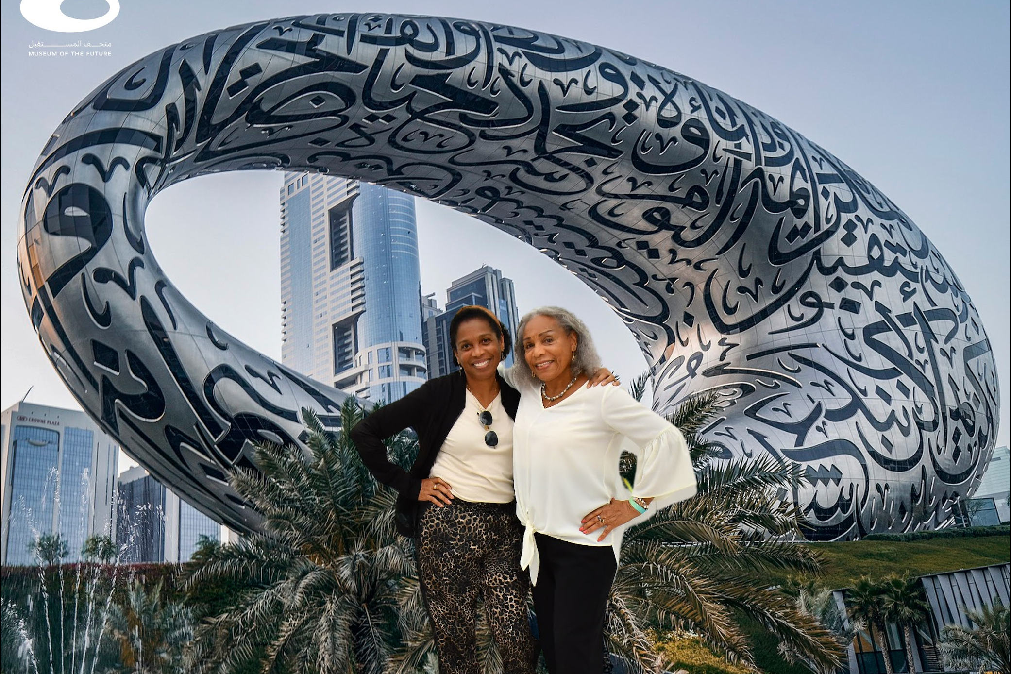 Advisor and friend posing in front of an outdoor, and large, silver, oval-shaped sculpture, decorated with Arabic writing, at The Museum of the Future.