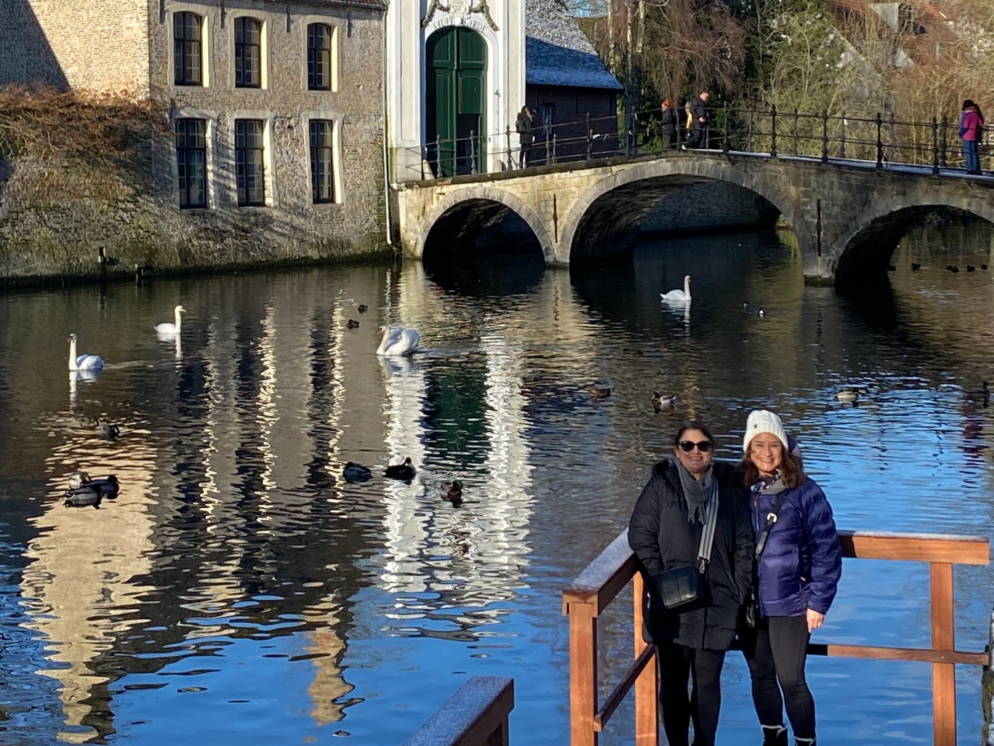Women standing in front of canal with ducks.