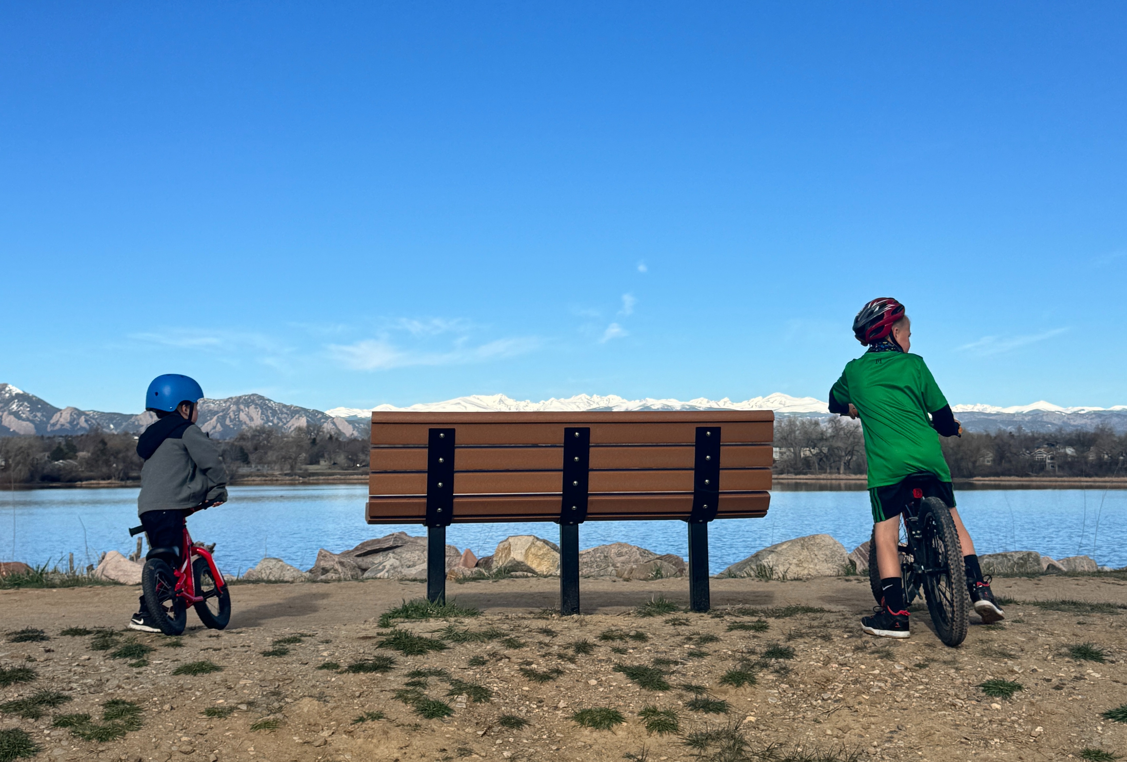 A view of two children on bicycles at the lake with the mountains of Colorado in the distance.