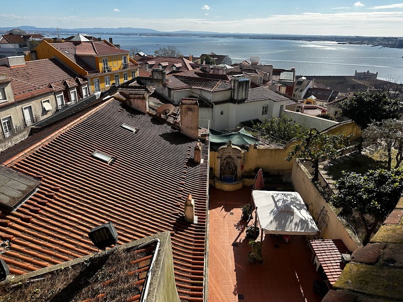 A view from above in the Alfama neighborhood of Lisbon overlooking rooftops of houses with the sea in the distance