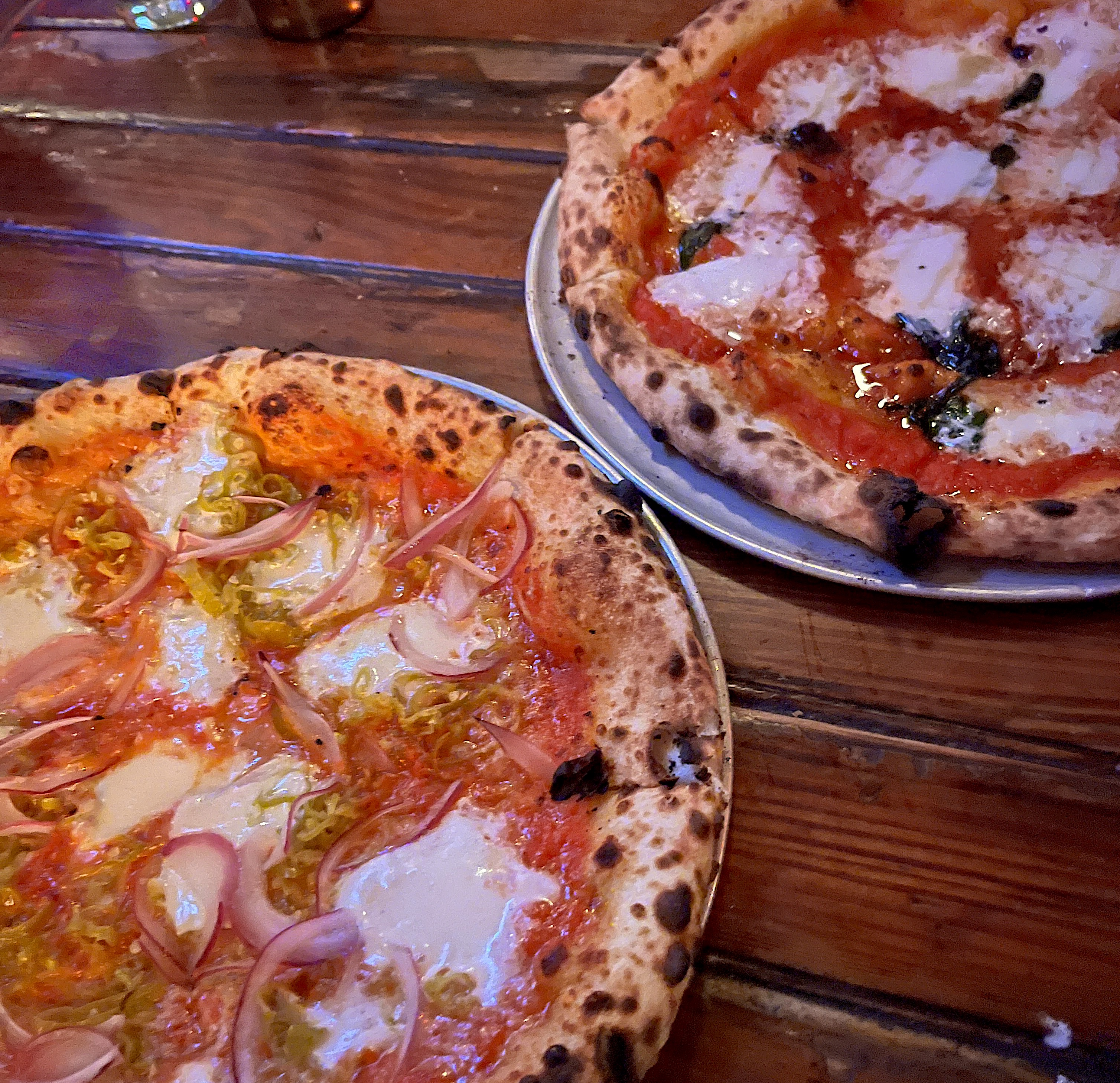 A wooden table with two pizzas on silver platters.