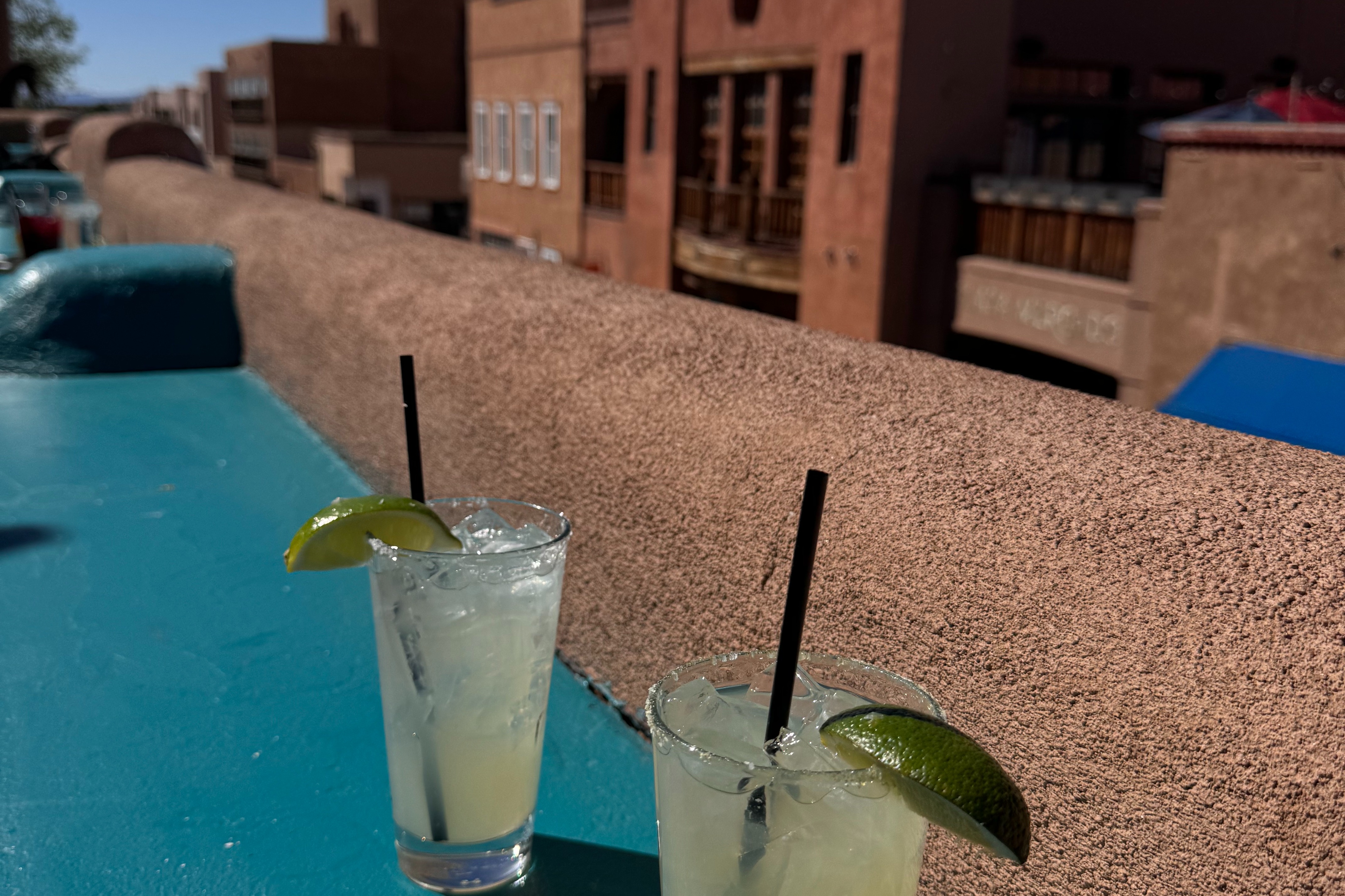 An image of two margaritas with lime on the bar by a stone ledge.