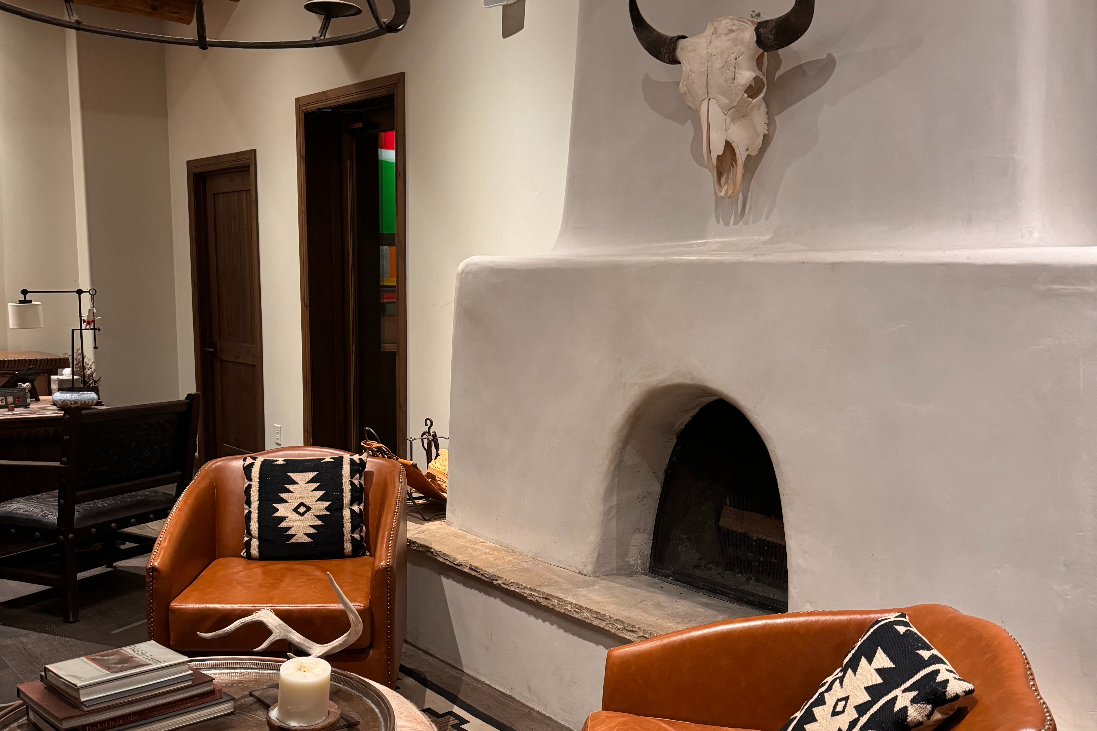 This image depicts a stone fireplace with a skull mounted onto the wall, two leather chairs, patterned pillows and furniture in the surrounding area.