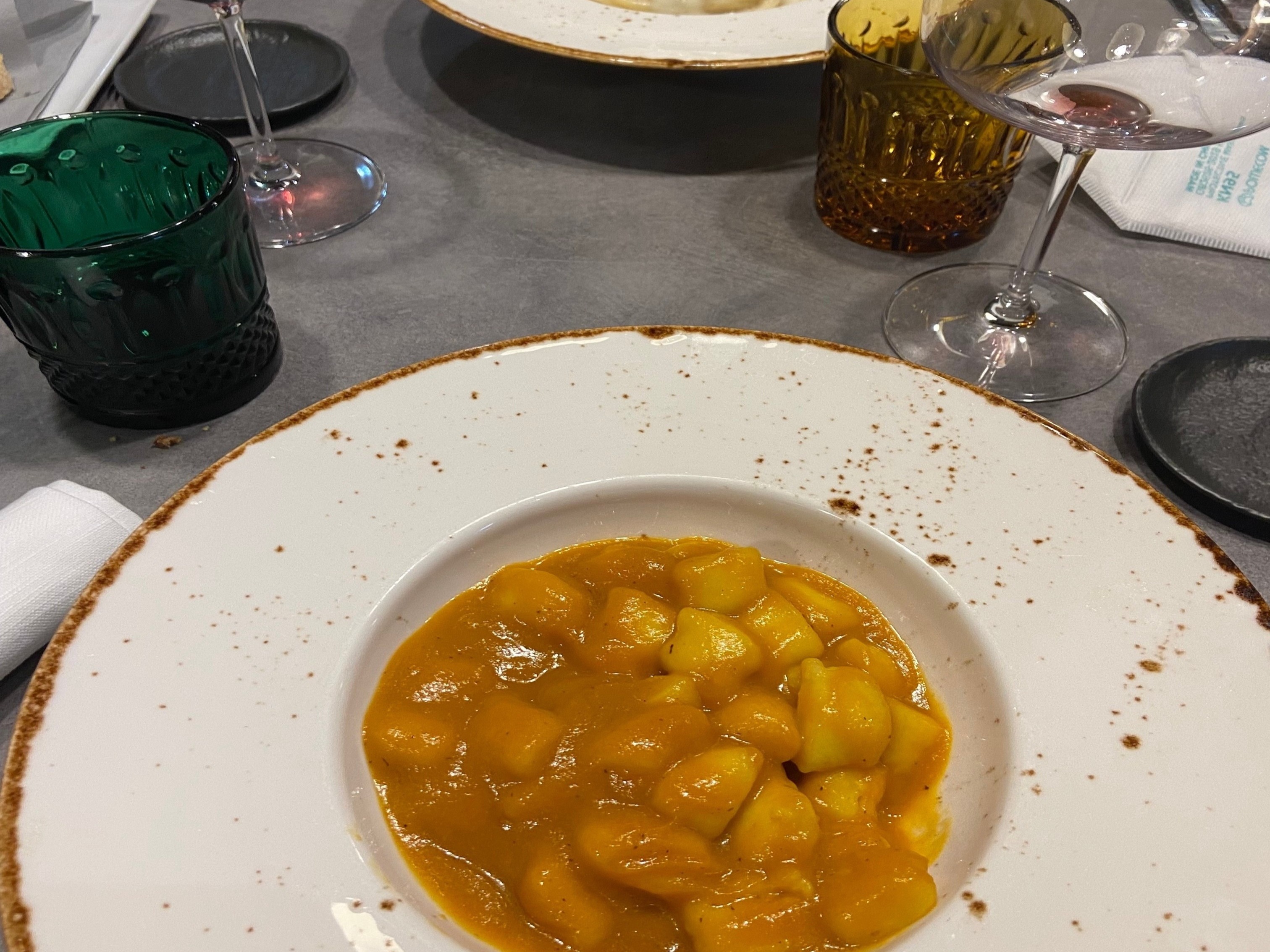 A formal dining setting with a plate of diced yellow fruit in sauce, accompanied by wine and cream on a well-set table.