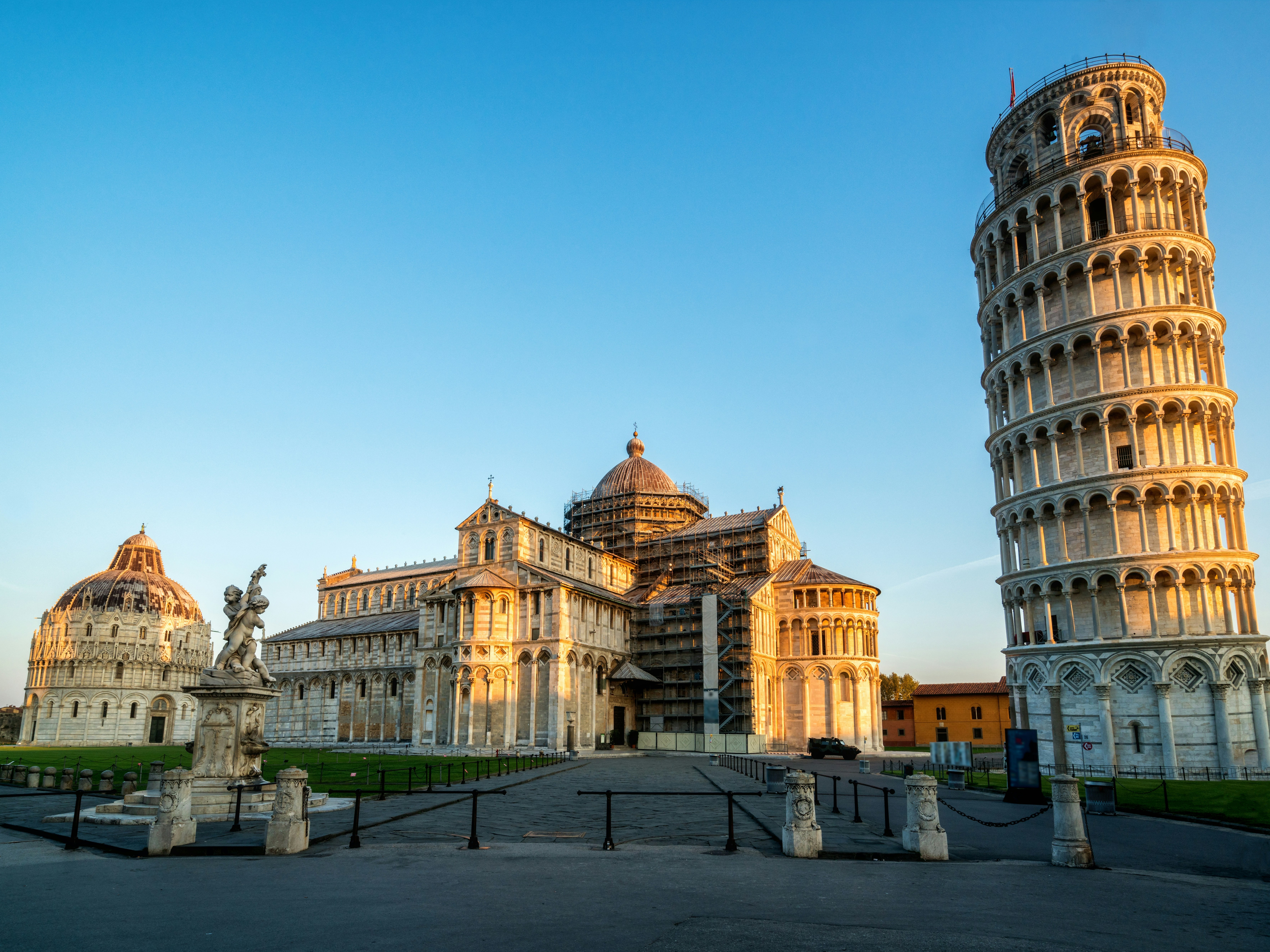 The image captures the iconic Leaning Tower of Pisa during golden hour, alongside the Pisa Cathedral and Baptistery, in a serene square.