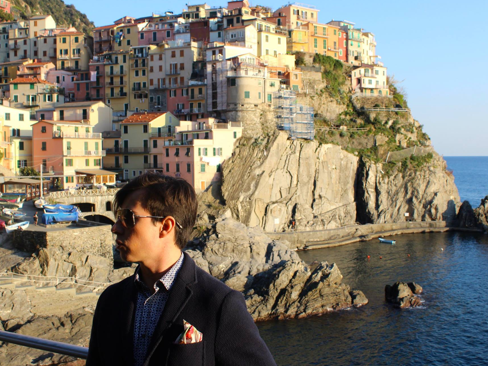 The image presents a picturesque coastal scene with colorful cliffside buildings and a person in the foreground, overlooking a serene sea.
