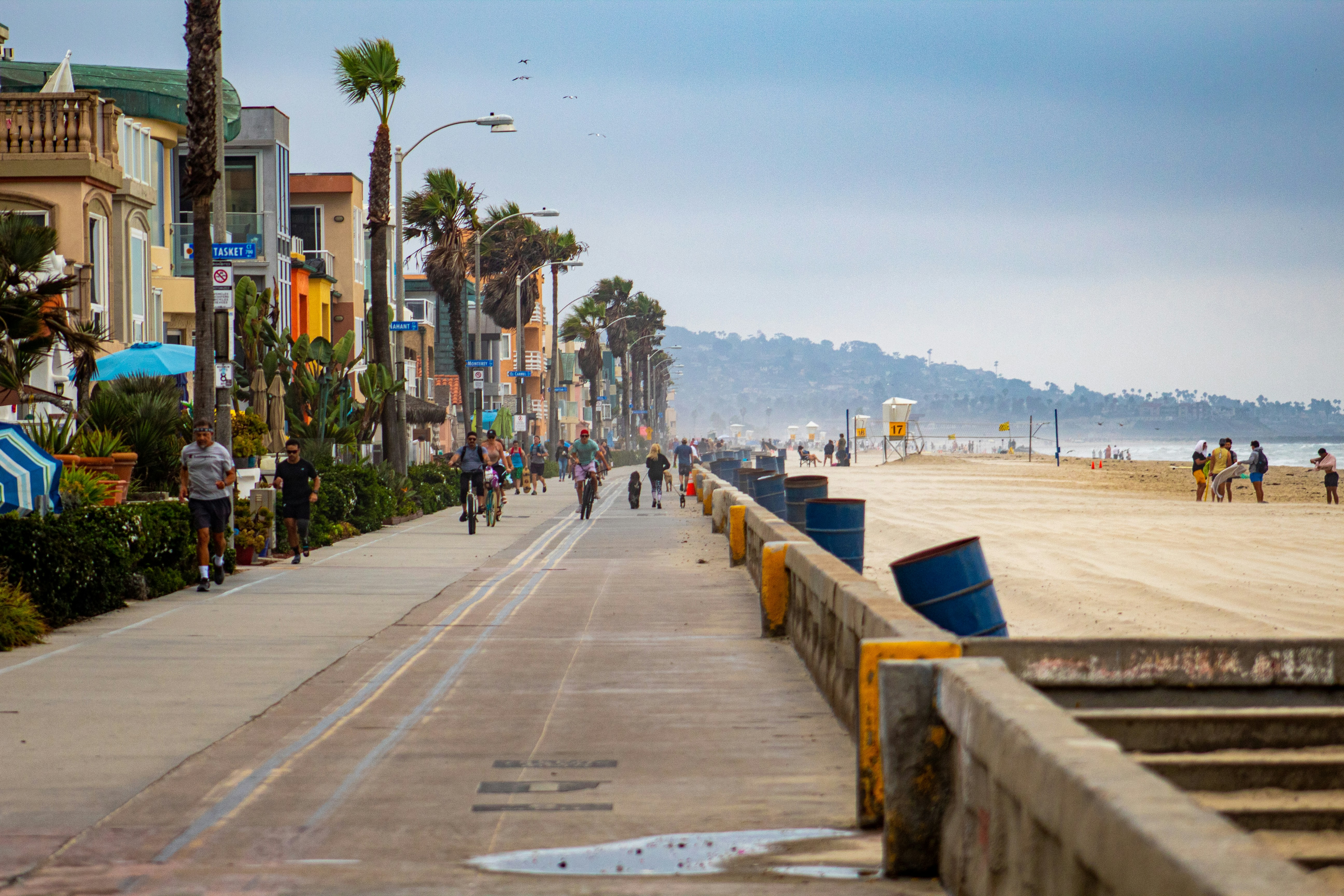 The boardwalk at Mission Beach with the ocean on one side and people walking and biking on the other next to palm trees and buildings.