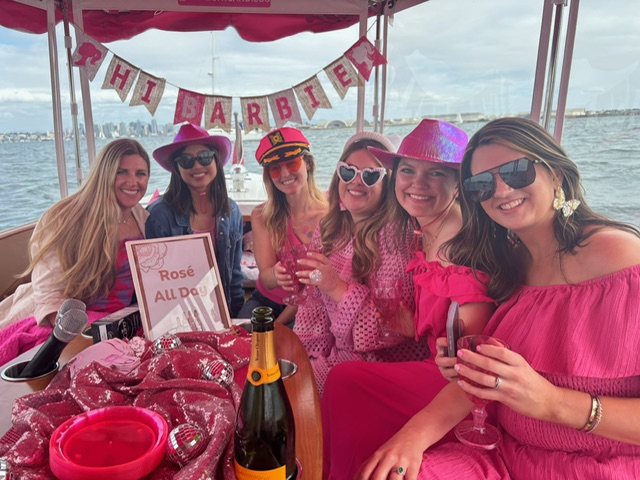 The bride-to-be and with a group of her girlfriends, all dressed in pink, sharing drinks and laughs, on a boat in San Diego during the daytime.