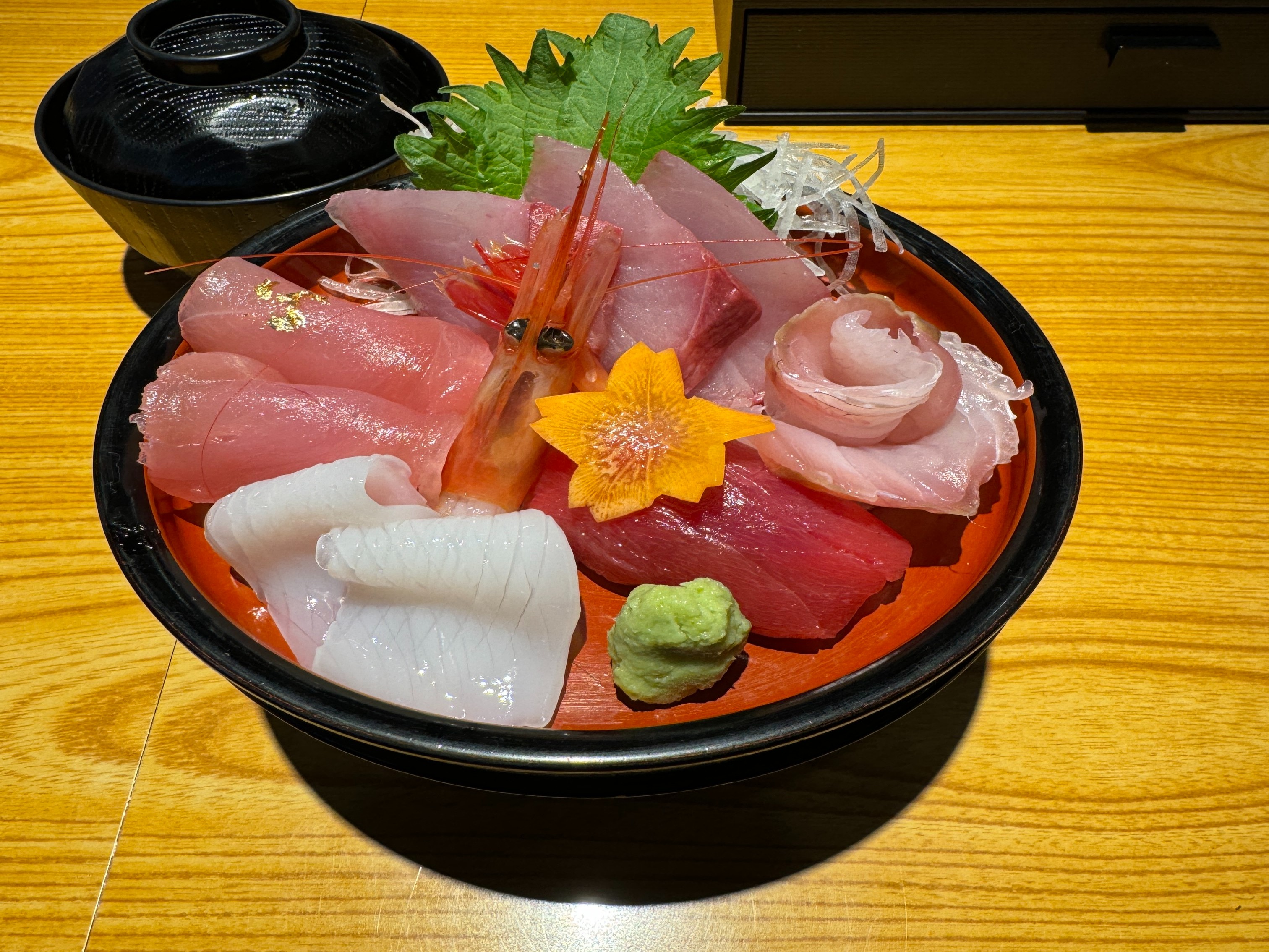 Sashimi arranged in a black bowl on a wooden table.