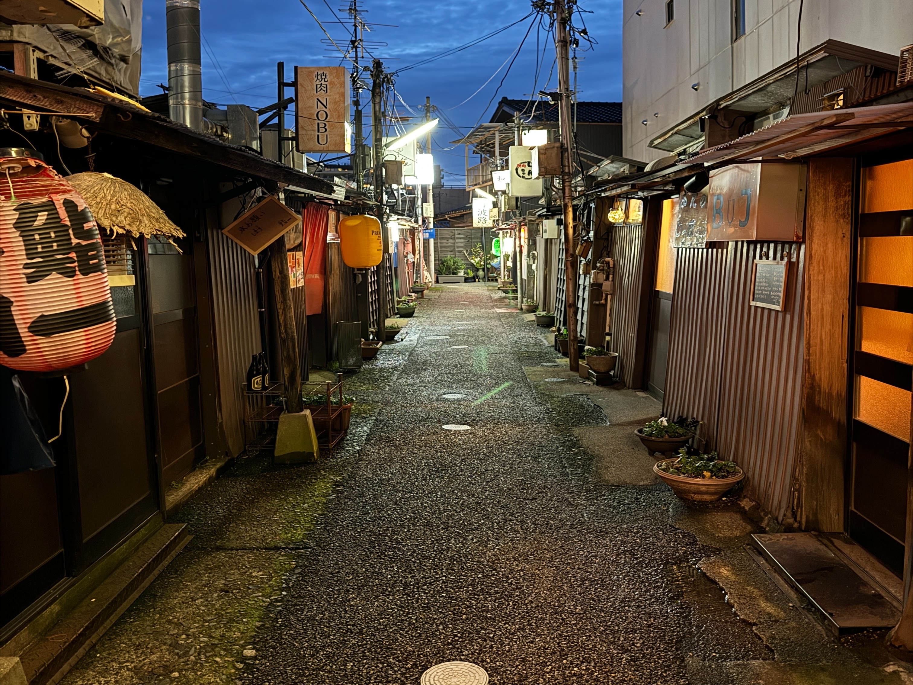 An alleyway at dusk, illuminated by the glow of lanterns and signs.