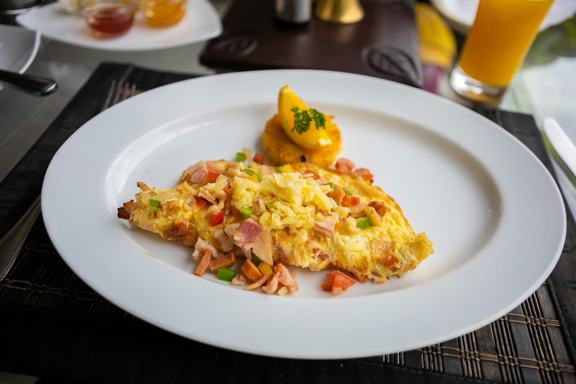 A freshly prepared omelet with meat and vegetable toppings on a white, ceramic plate at an outdoor restaurant.