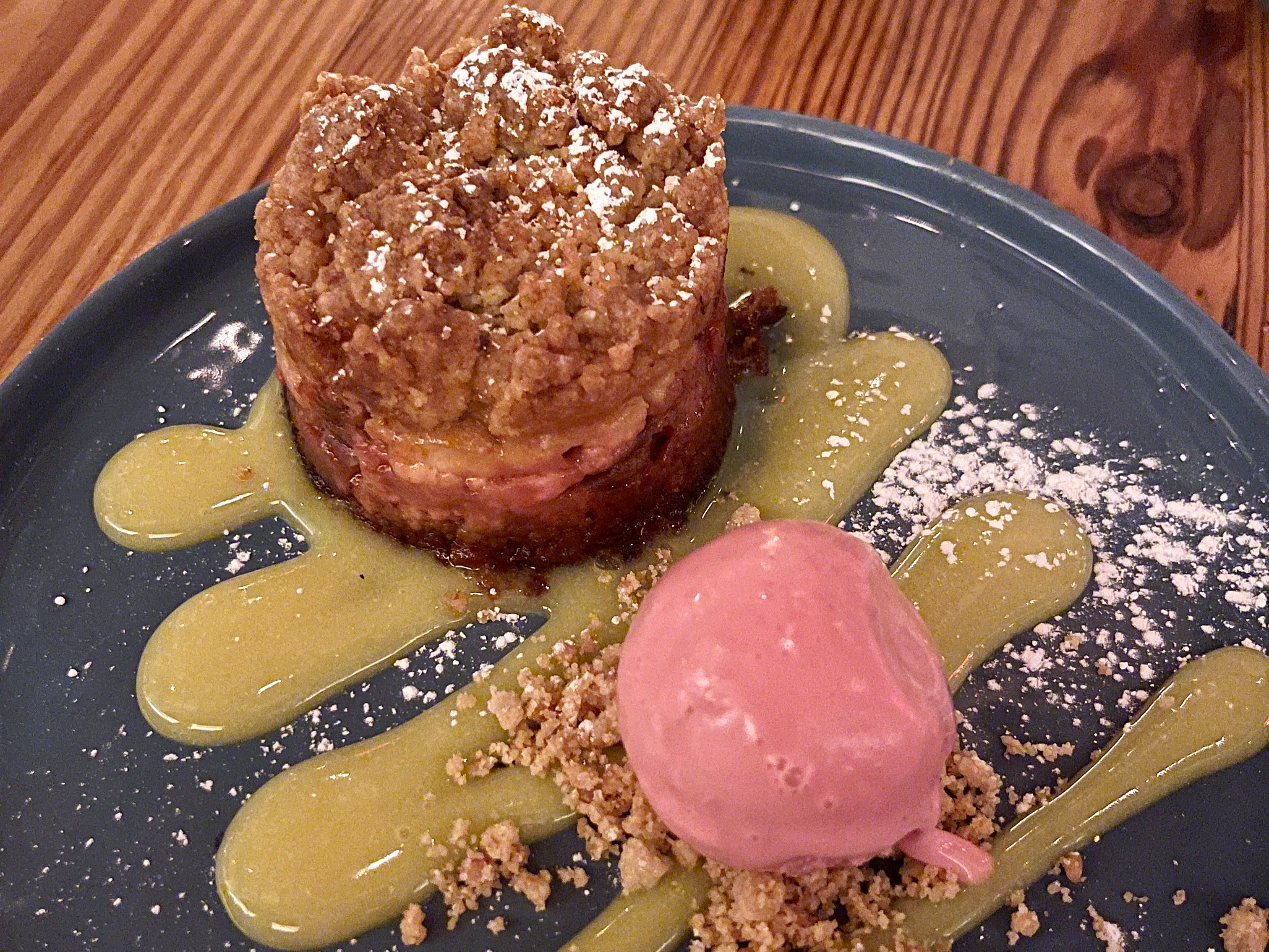 An elegant dessert at meadowsweet, a pastry and a scoop of pink ice cream with green sauce on a blue plate.