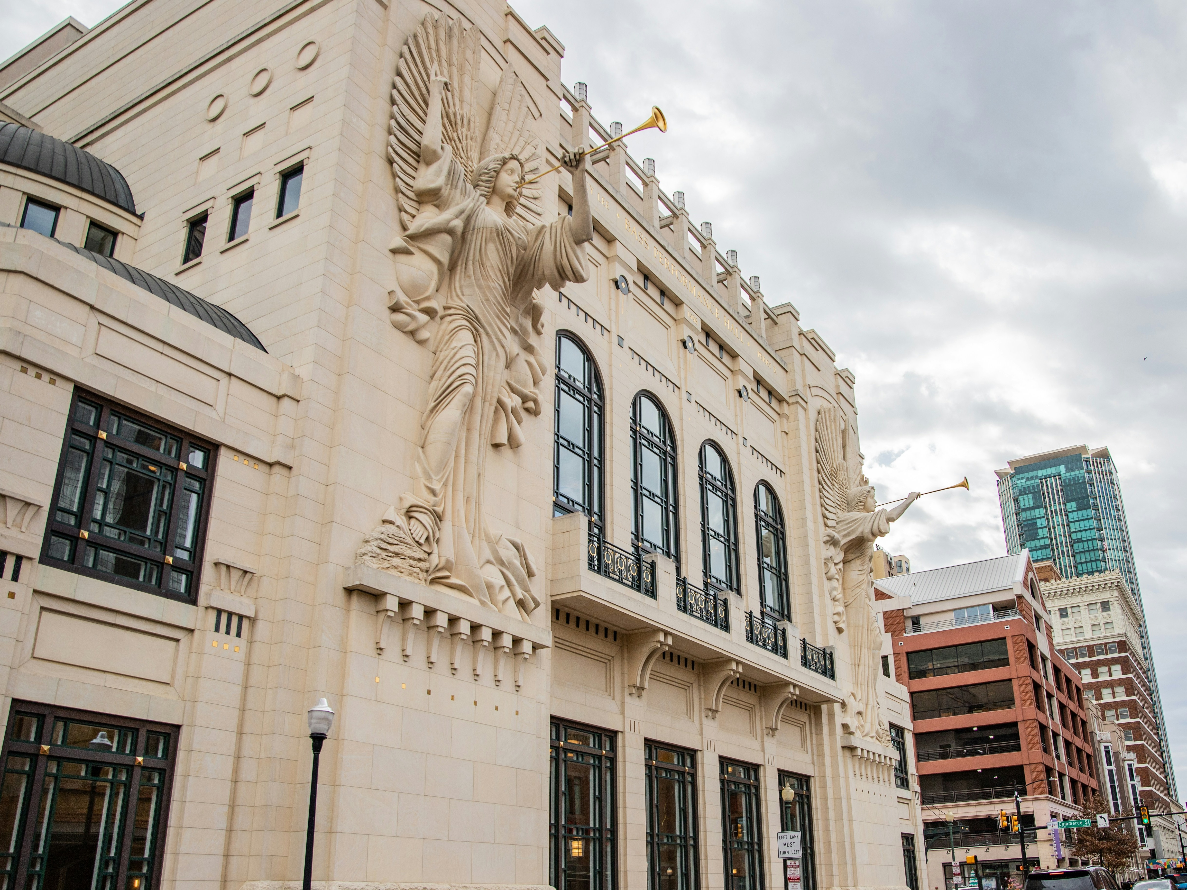 The image showcases a winged sculpture with a trumpet, mounted on a building’s facade against a clear blue sky.