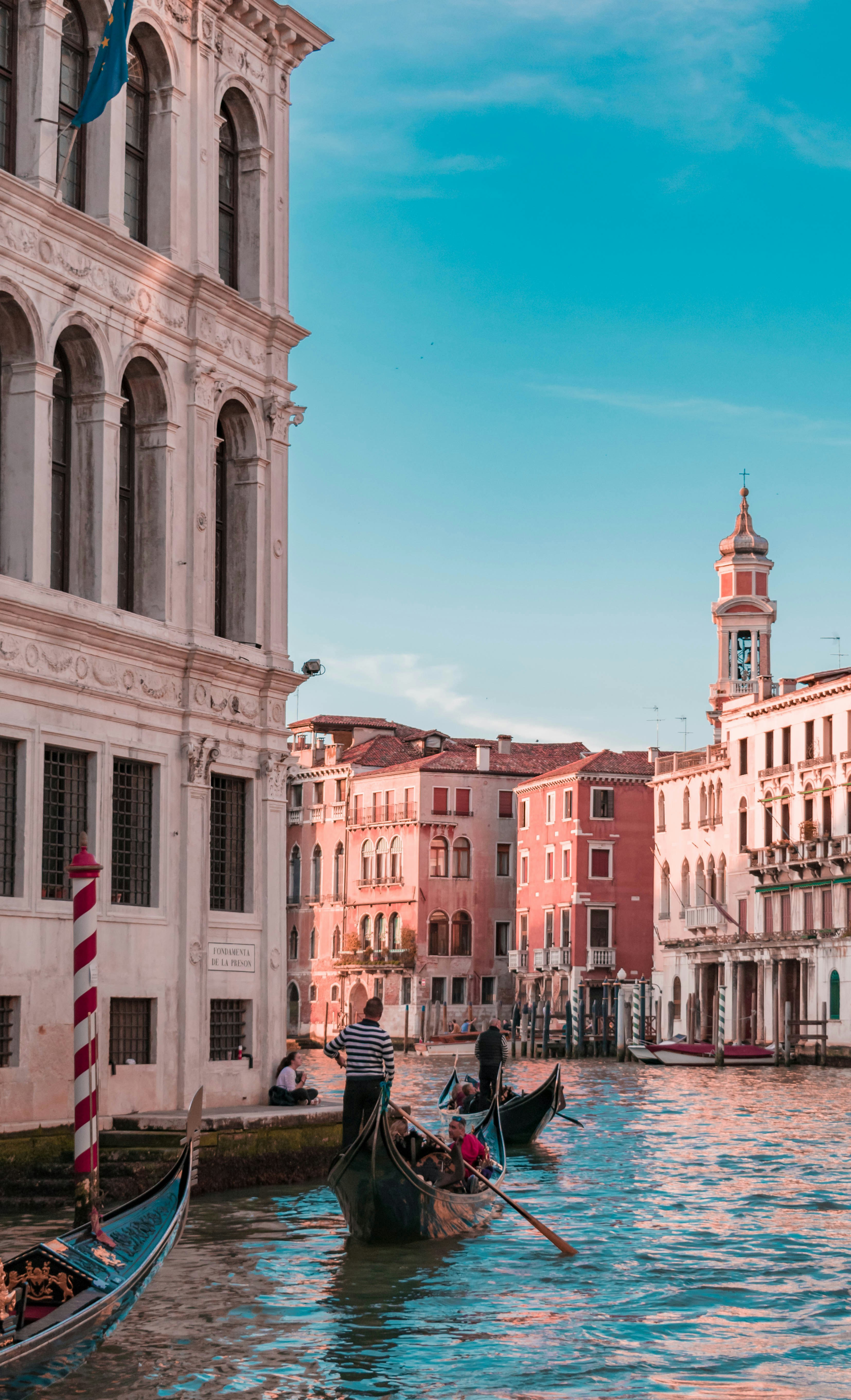 Venetian gondolas and gondoliers transporting tourists through Venice's canals, with classic architecture and buildings to view along the way.