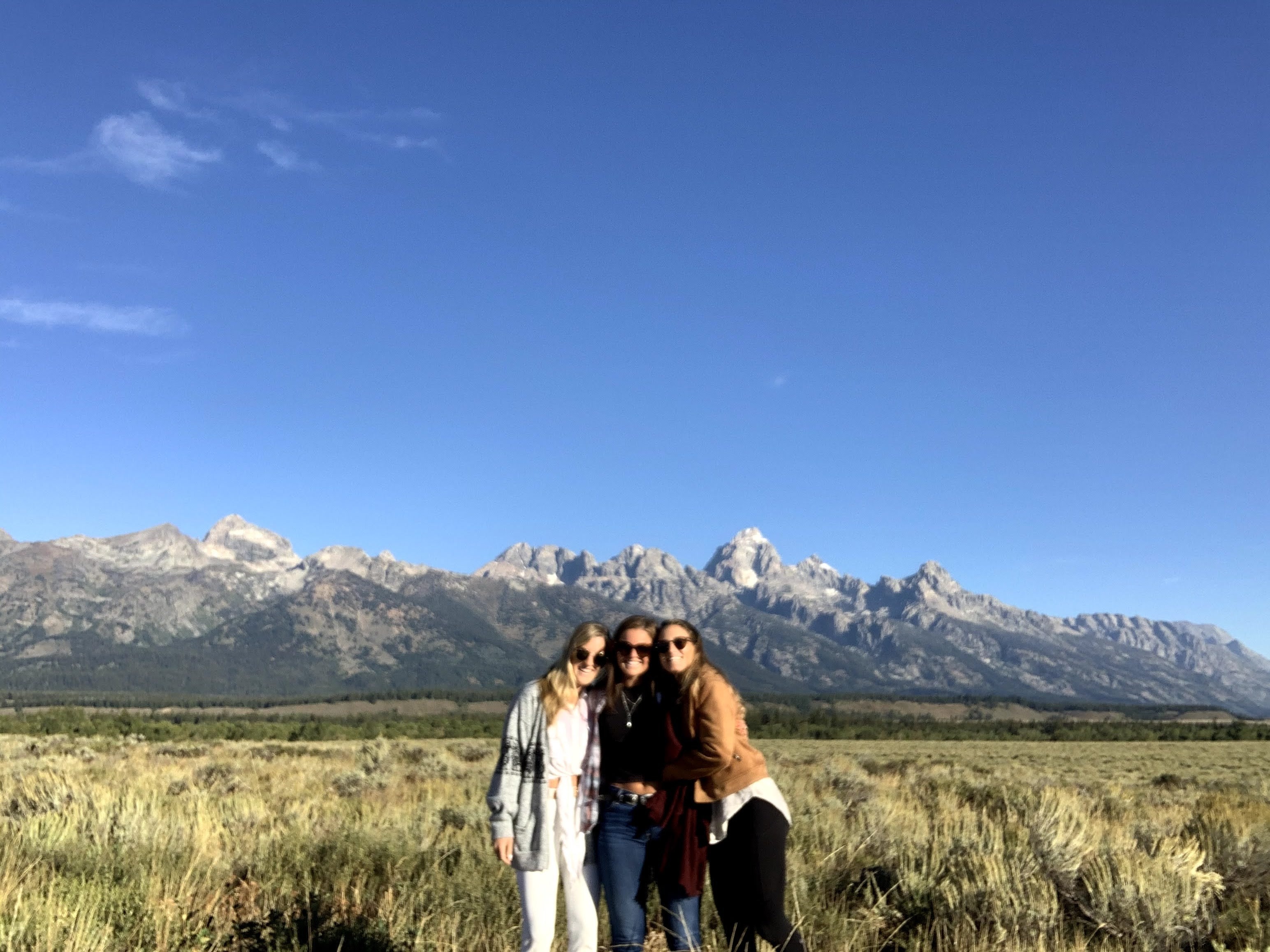 Tori and her friends in sunglasses standing with their arms around each other in front of mountains on a clear day.