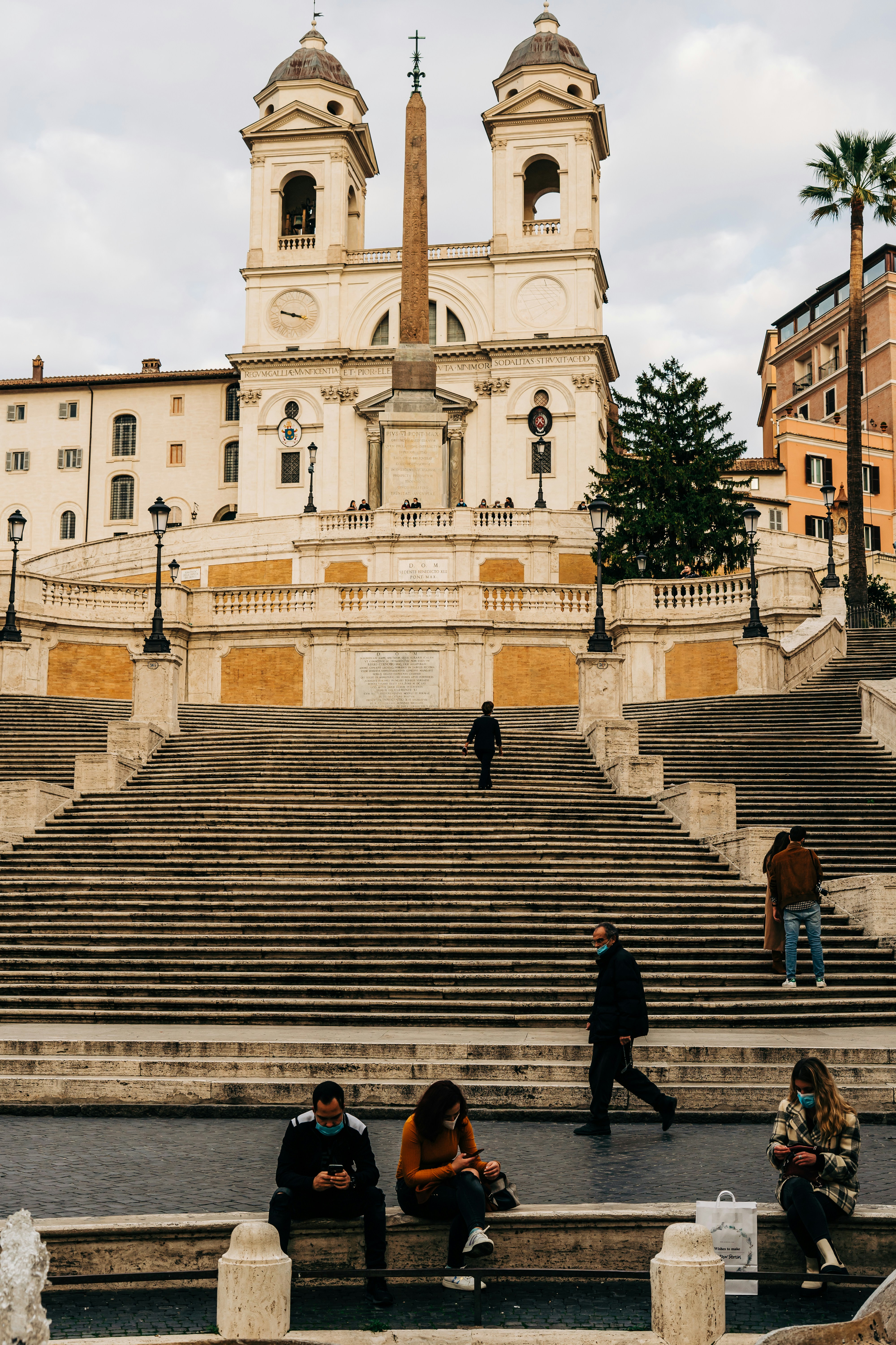 A look at the famous Spanish Steps in Rome, with a few people walking up the steps, and others sitting on a bench in front