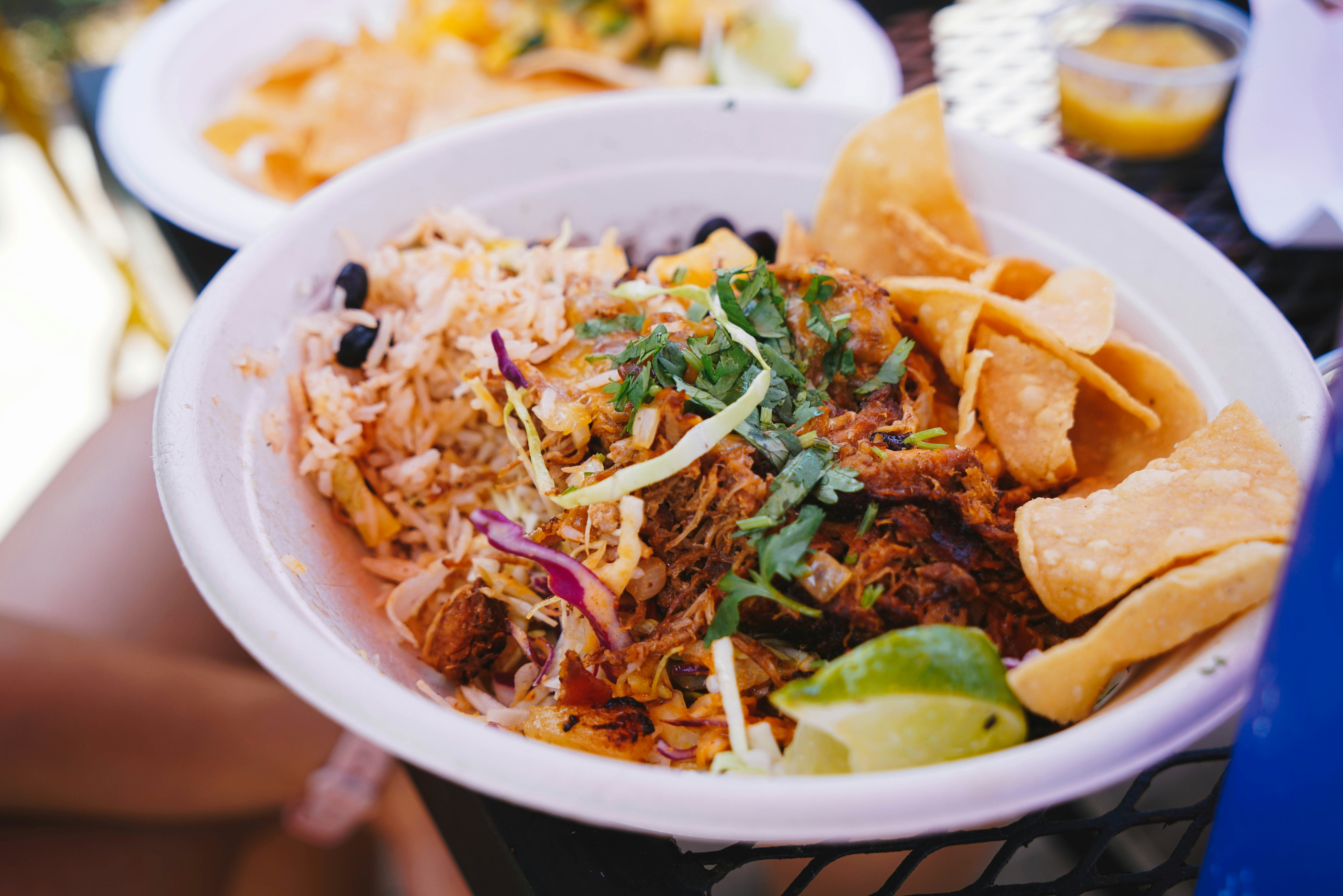 A white bowl with meat, rice and chips.