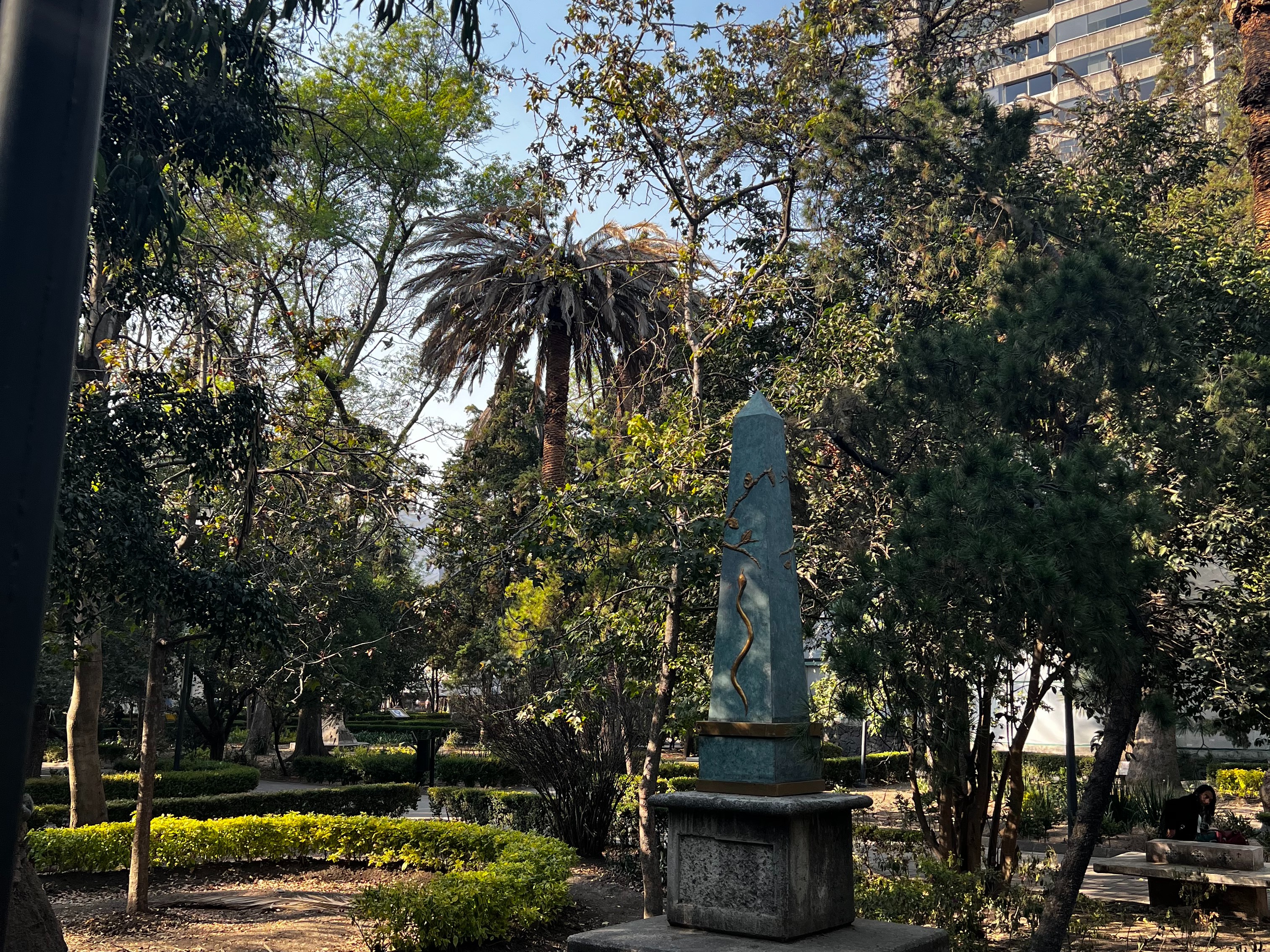 A picture of green trees and a large statue in the middle of an outdoor park.