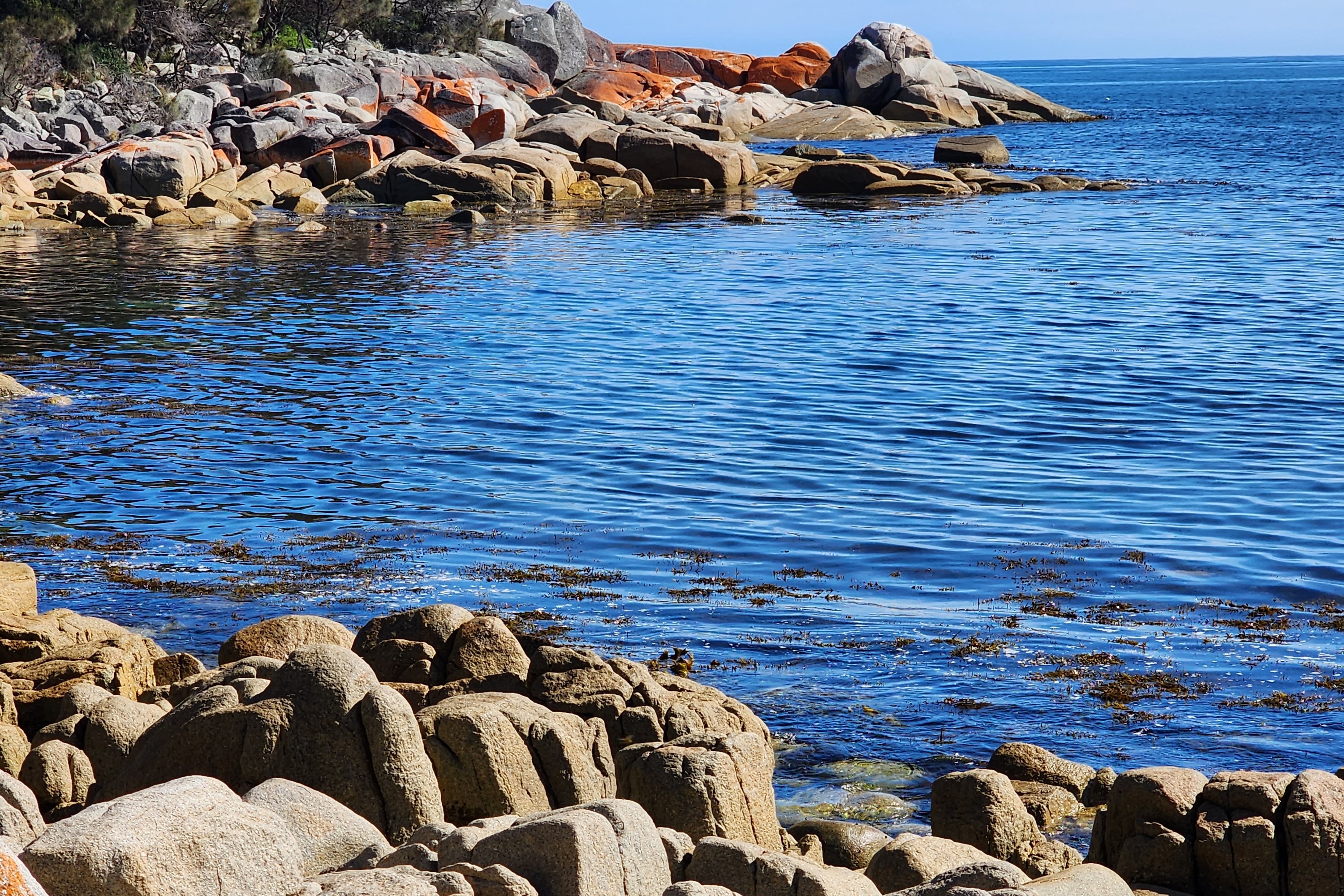 The Bay of Fires, a blue bay surrounded by rocks with an orange tint.