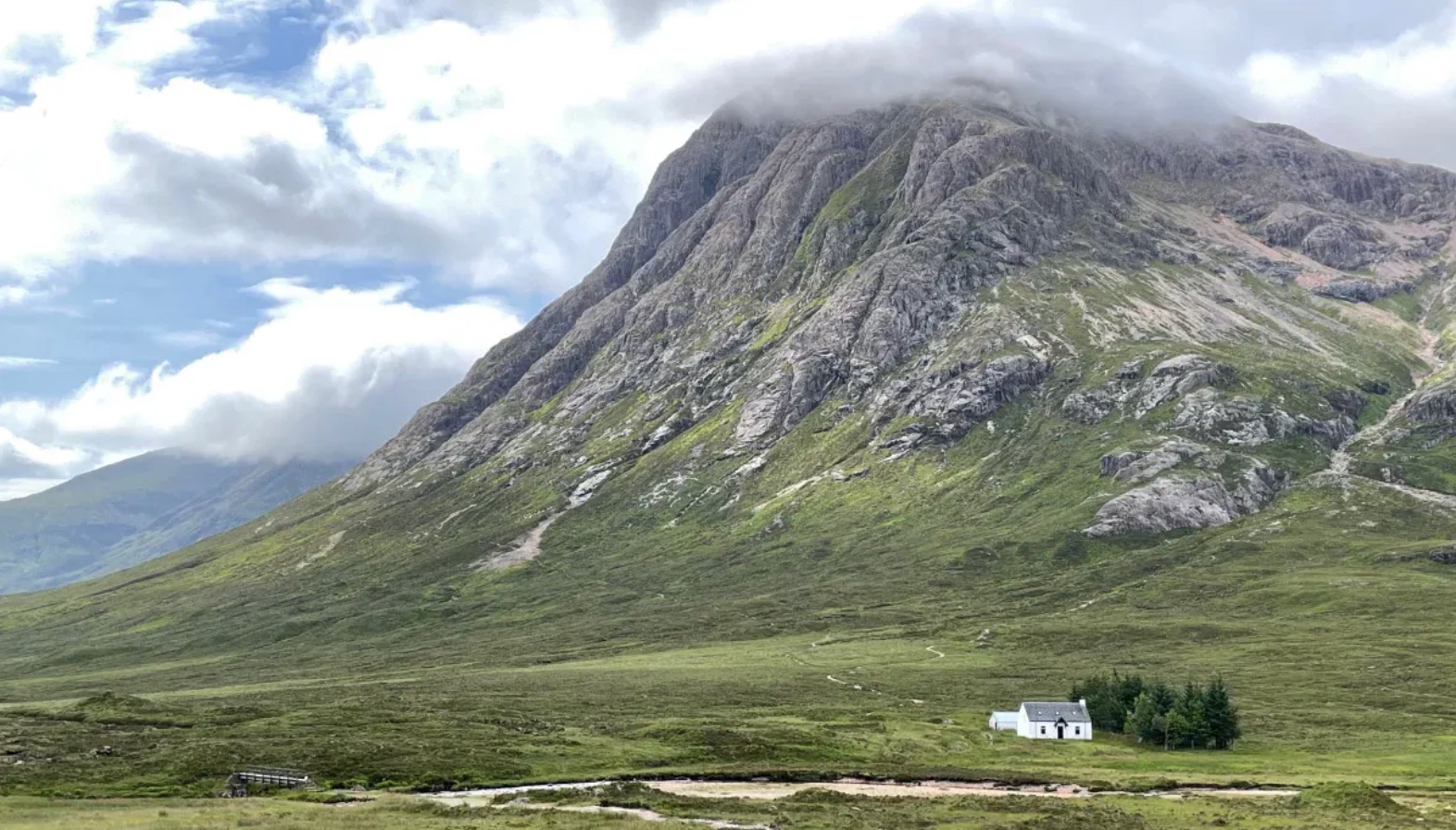 A small white house at he base of a very large mountain scape.